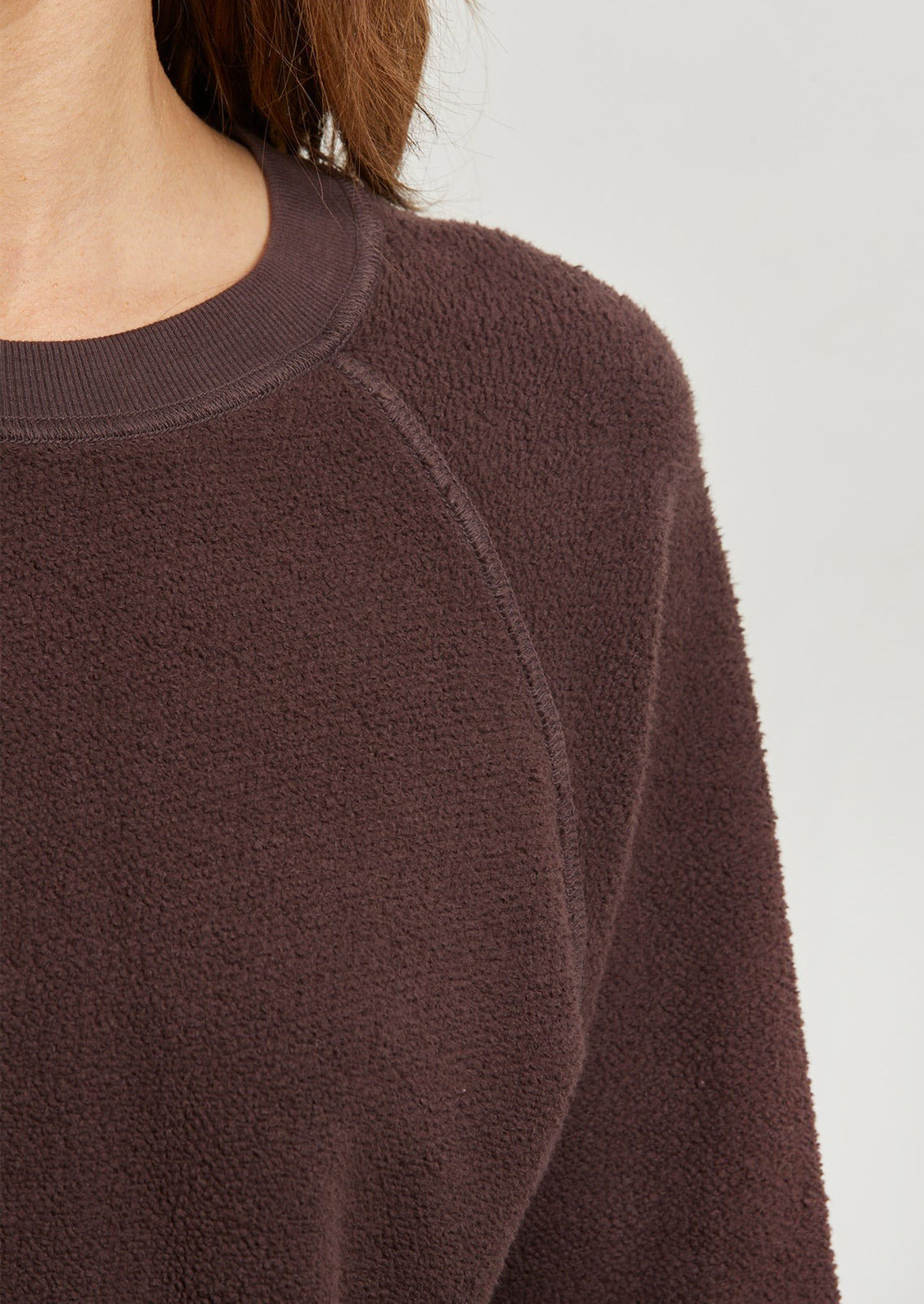 A woman wearing a brown crewneck sweatshirt.