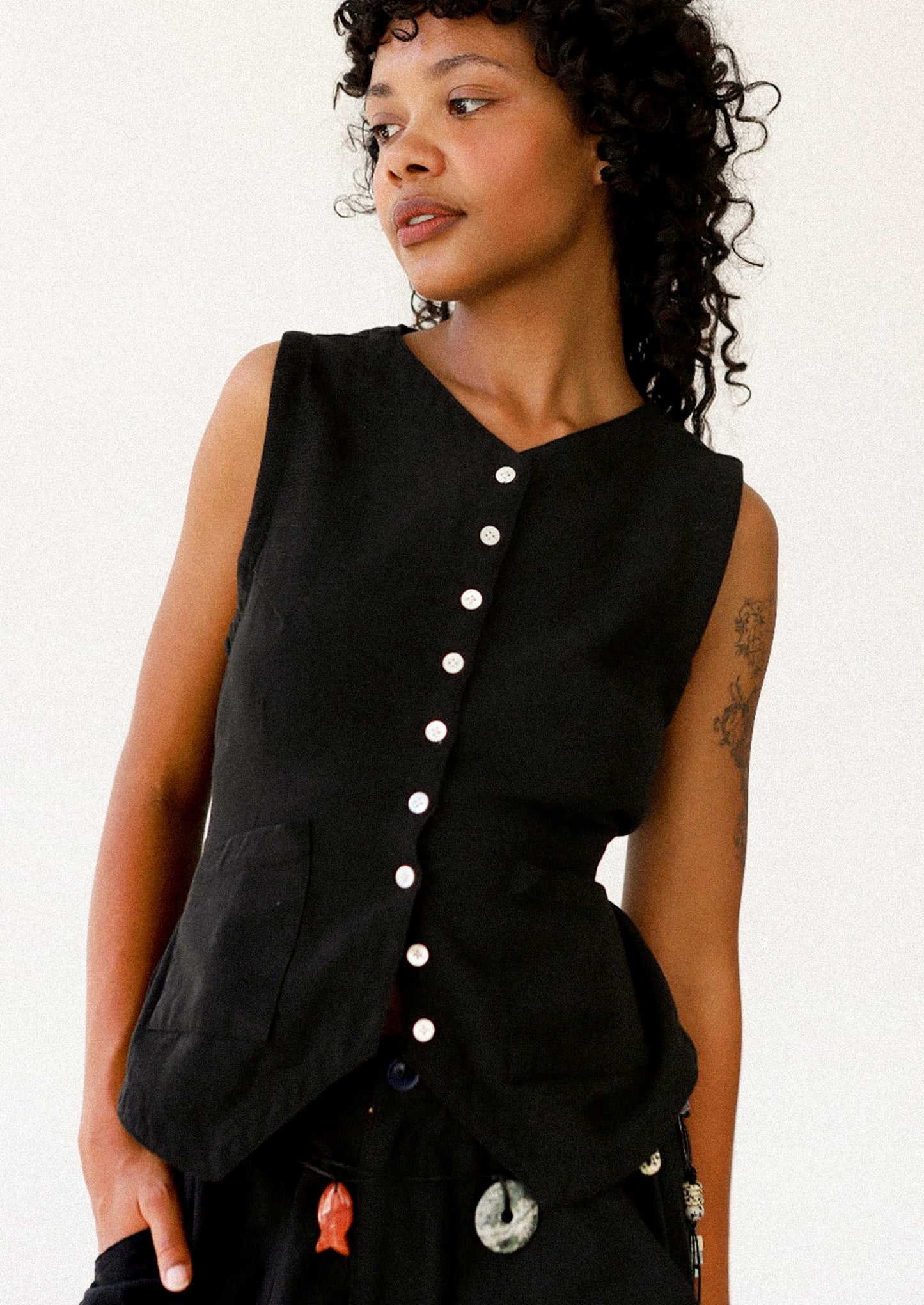 Woman wearing a black sleeveless top with buttons on a white background