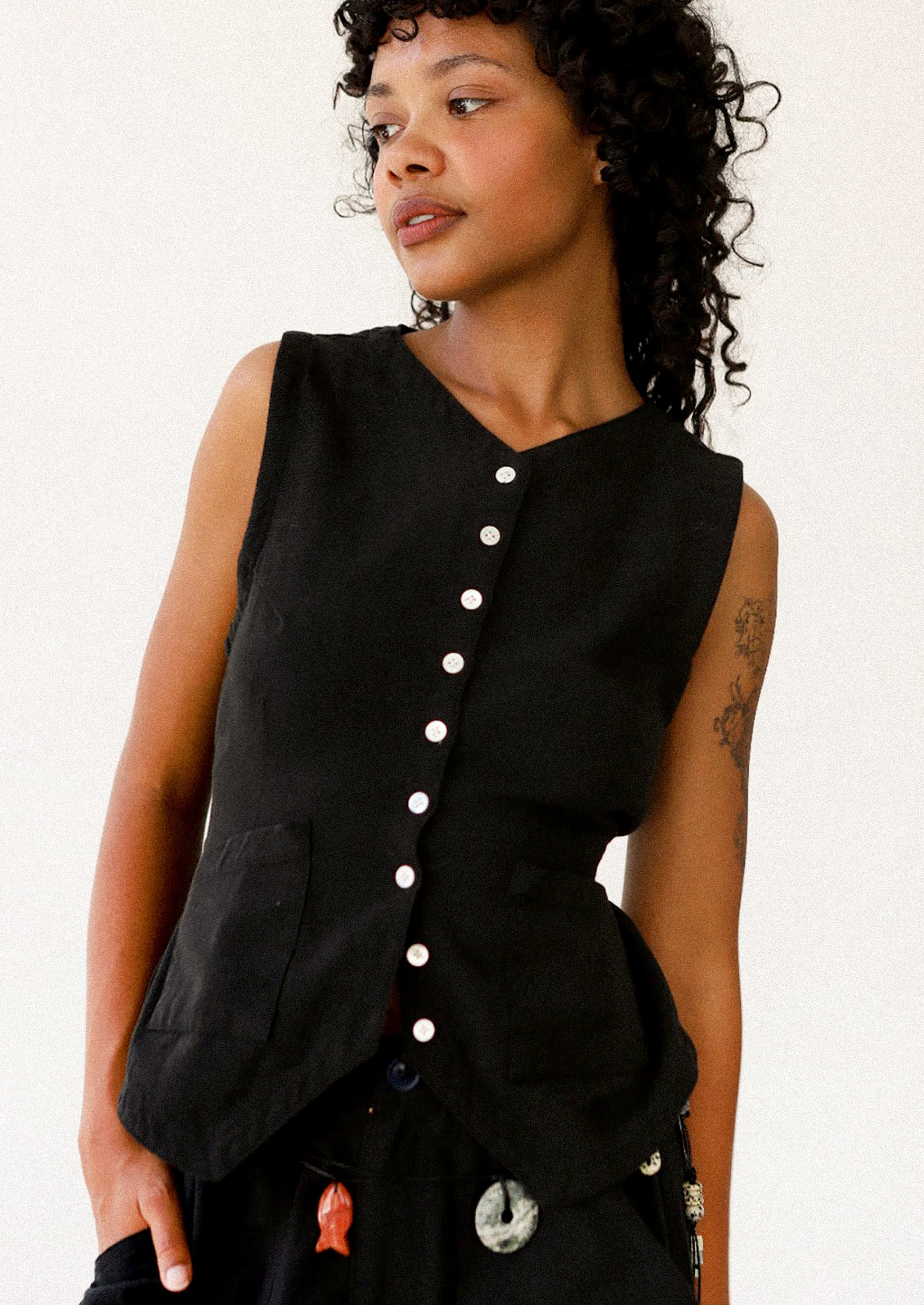 Woman wearing a black sleeveless top with buttons on a white background
