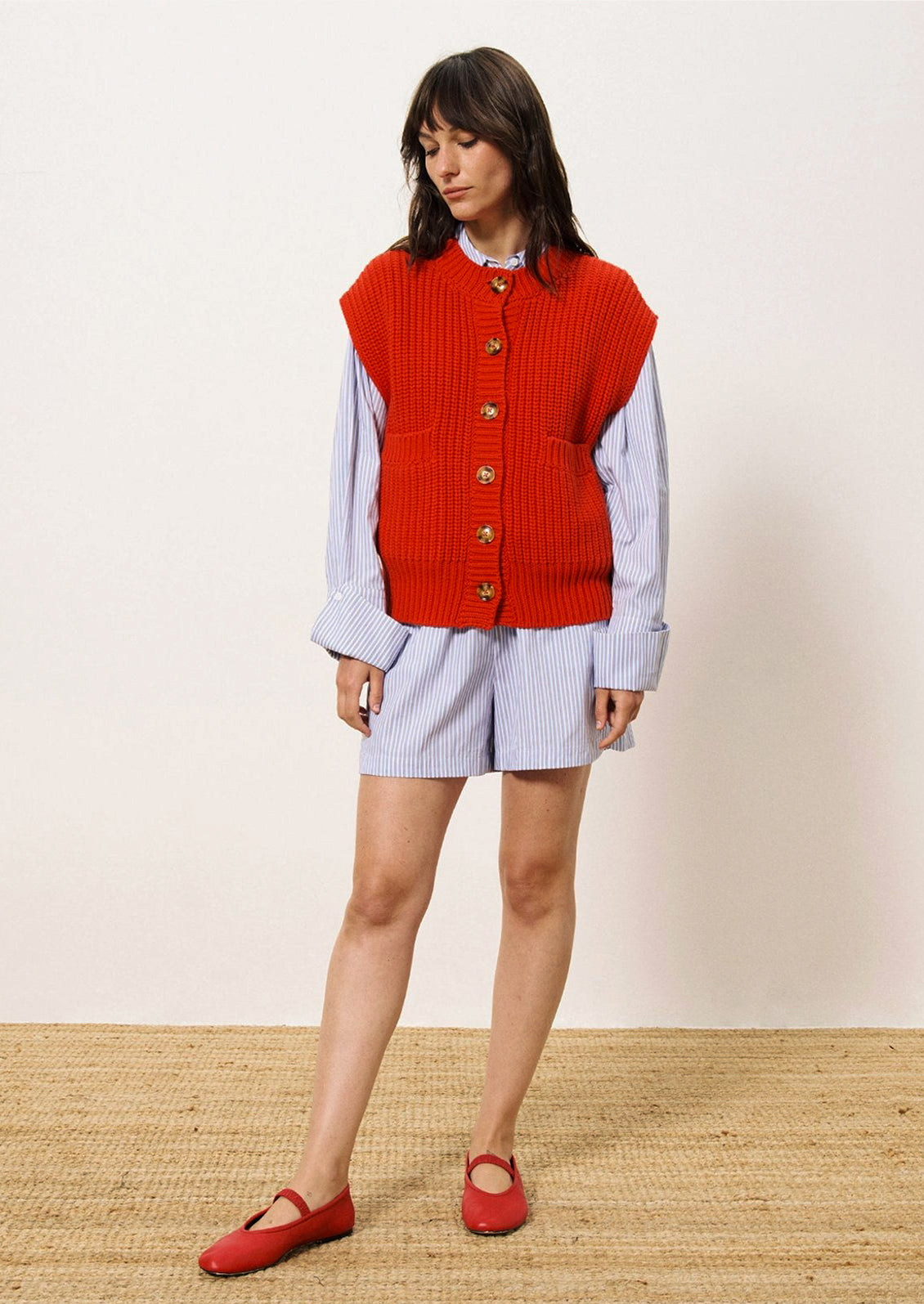 A person wearing a chunky knit button front sleeveless sweater vest in bright cherry red.