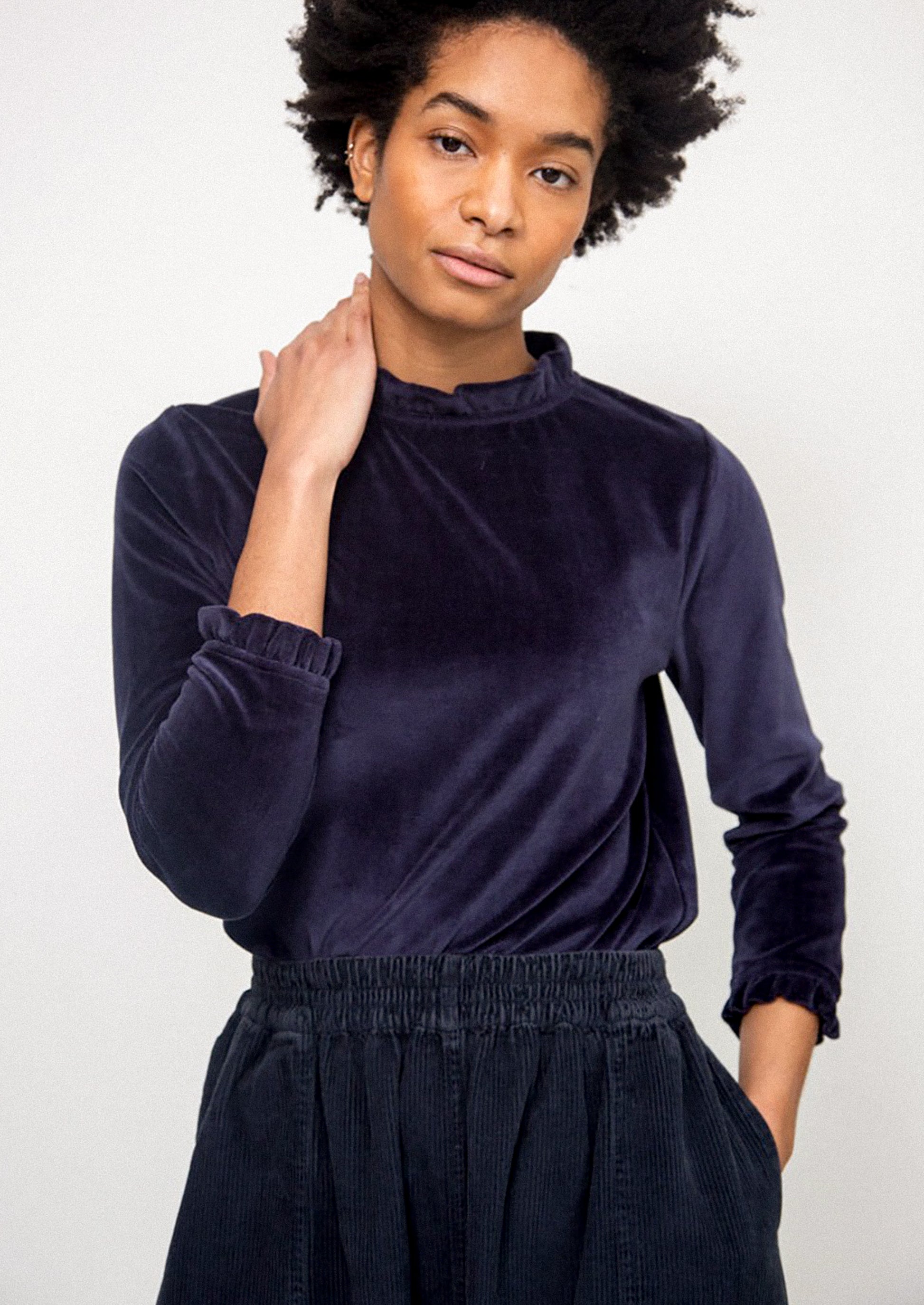 Woman wearing a dark blue velvet top and black pants against a white background