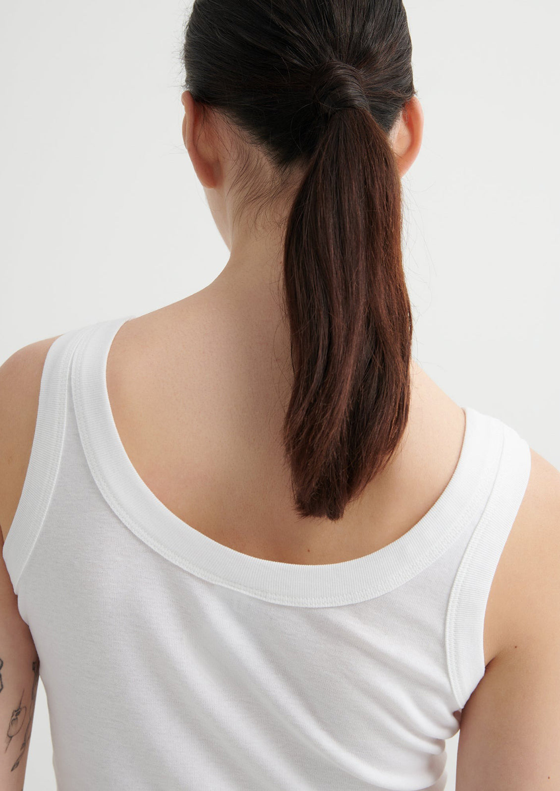 Person wearing a white tank top with a plain background