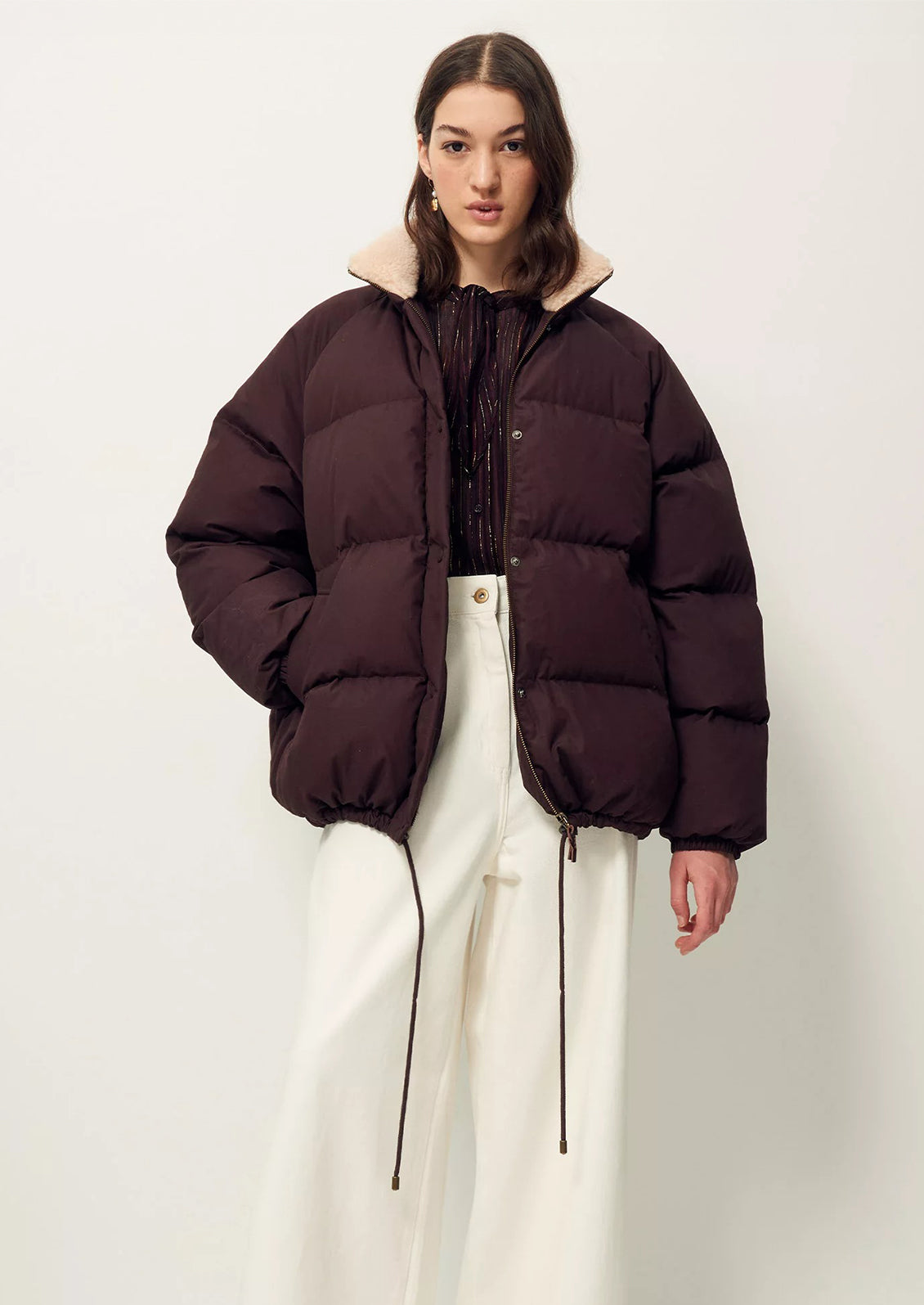 A woman wearing a burgundy puffer jacket with tan shearling collar.