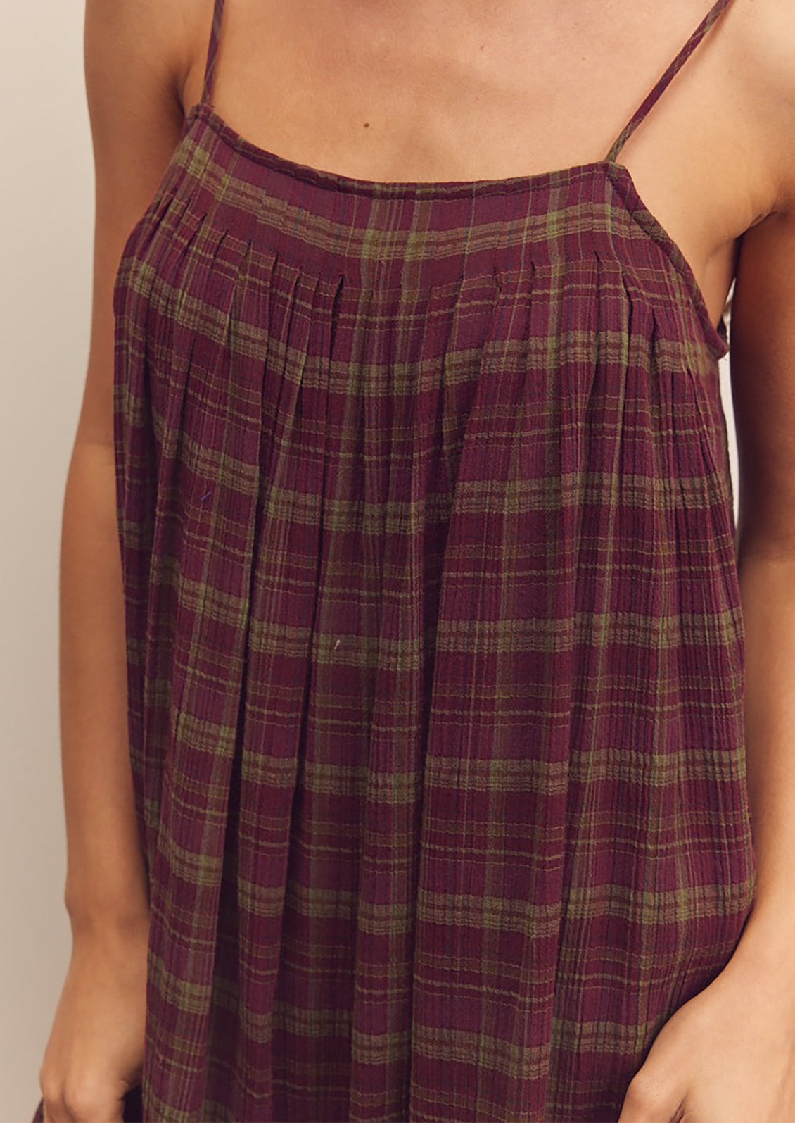 A person wearing a midi length dress in burgundy and green plaid pattern with thin straps.