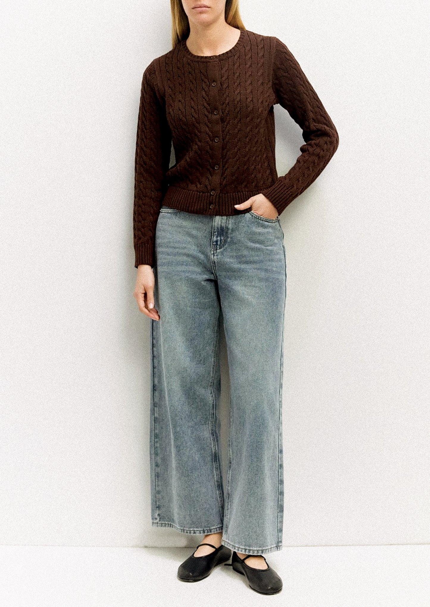 Person wearing a brown cable knit sweater and light blue jeans against a white background