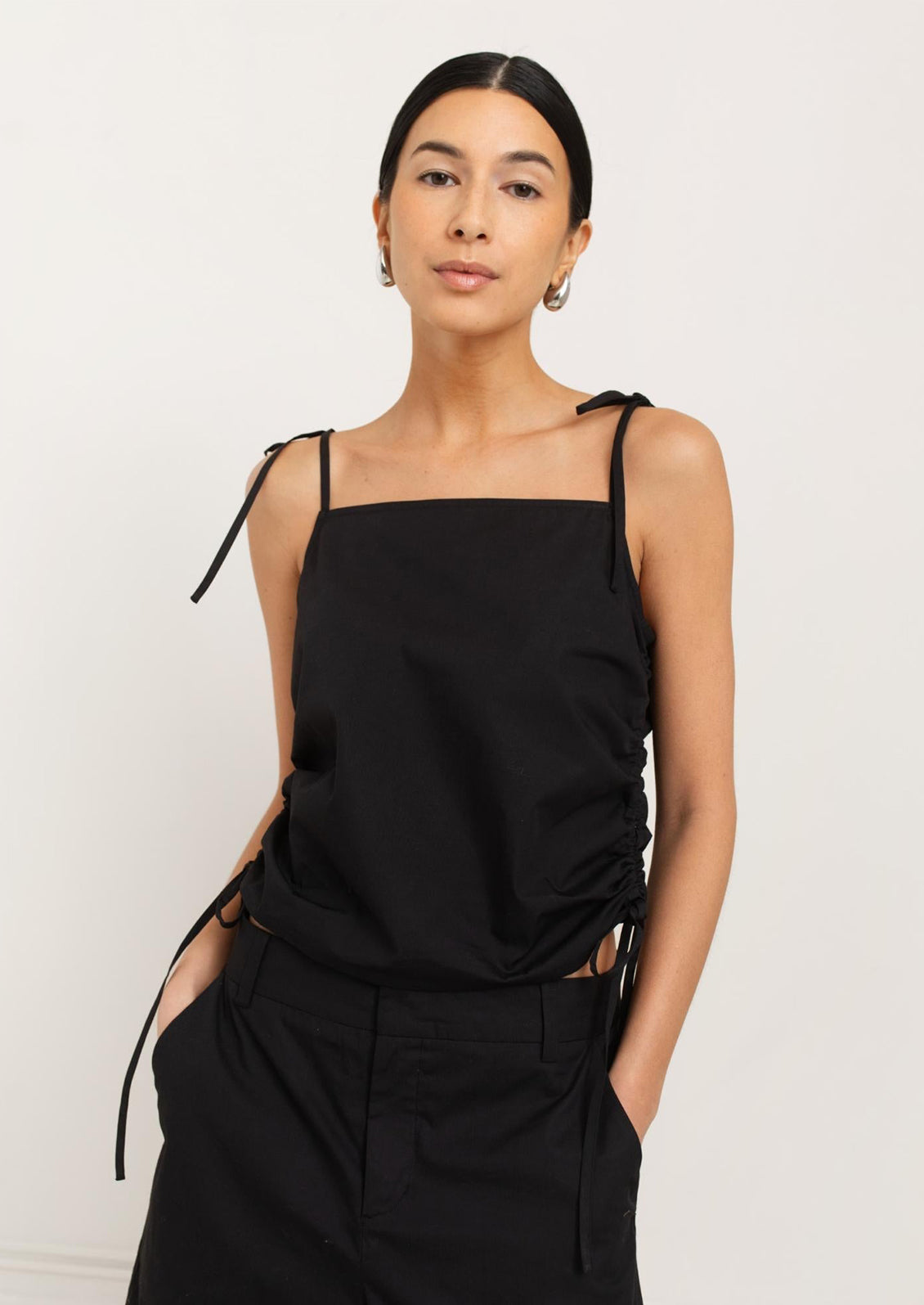 A woman wearing a black tank top with scrunched side detail.
