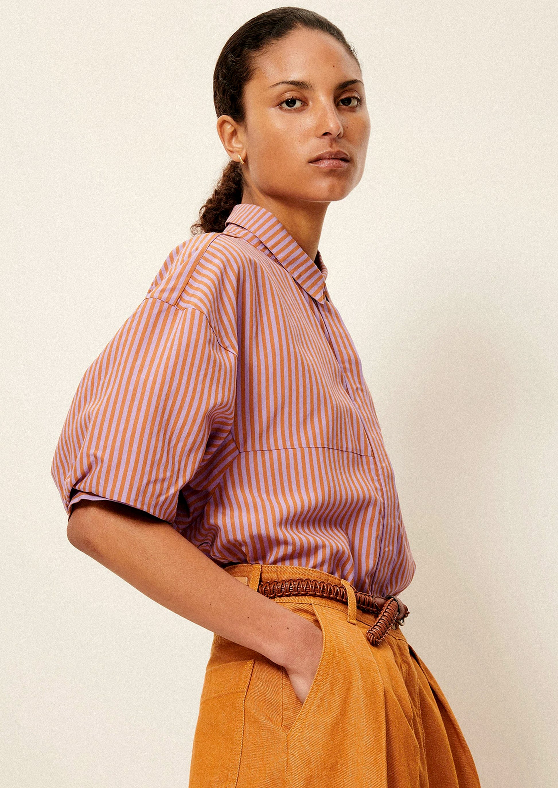 A woman wearing a short collared shirt in orange and purple stripes.