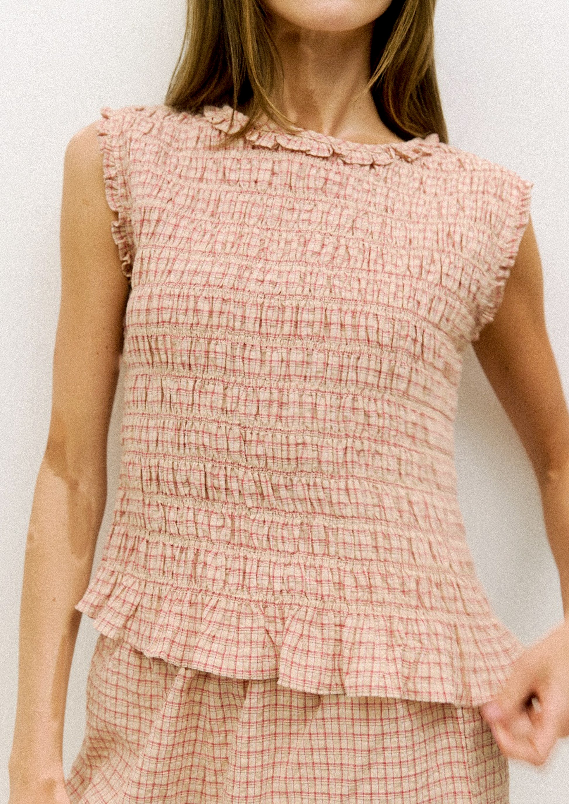 Woman wearing a pink checkered top with ruffled details on a white background