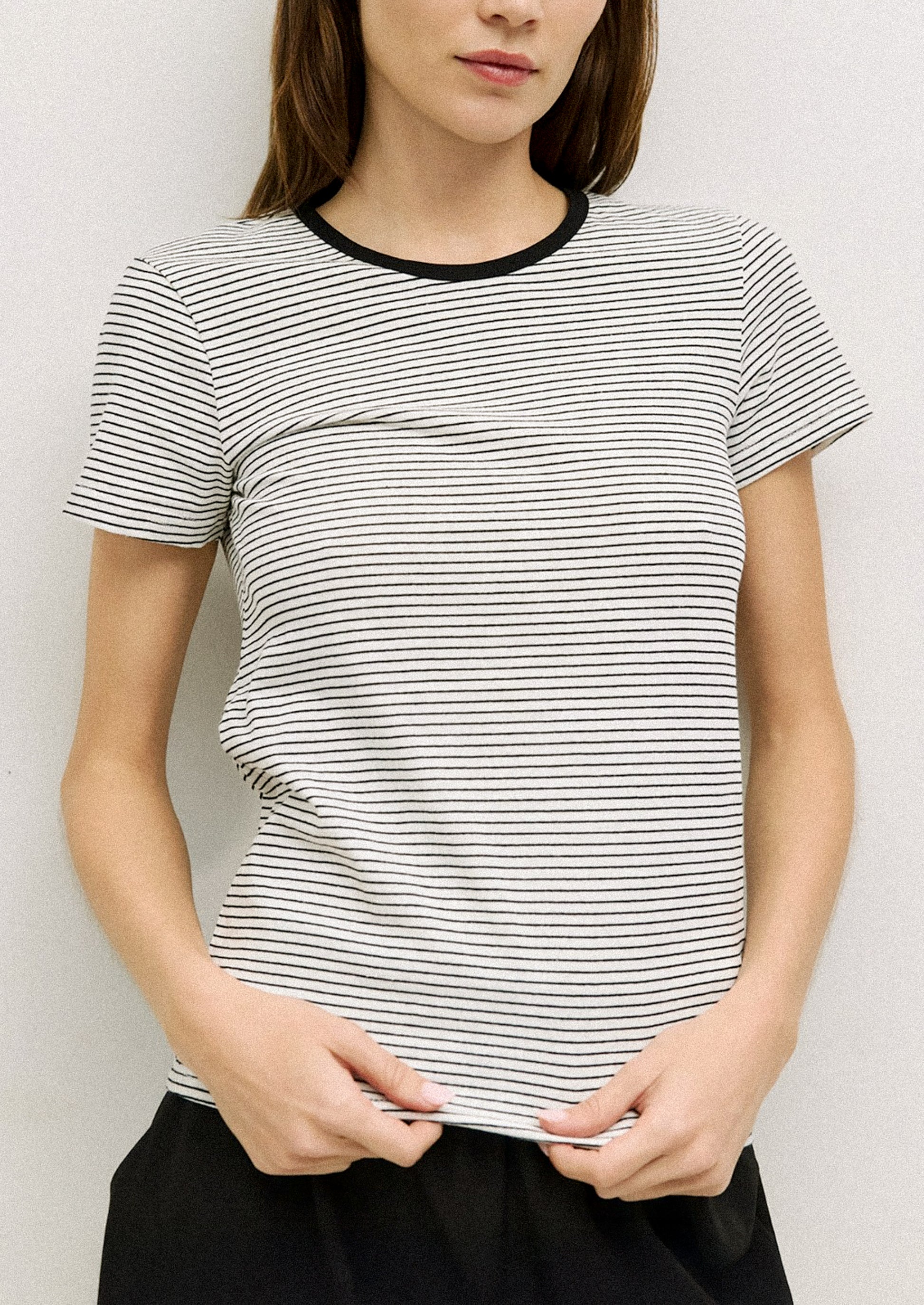 A person wearing a striped t-shirt in white with black stripes and neckline.