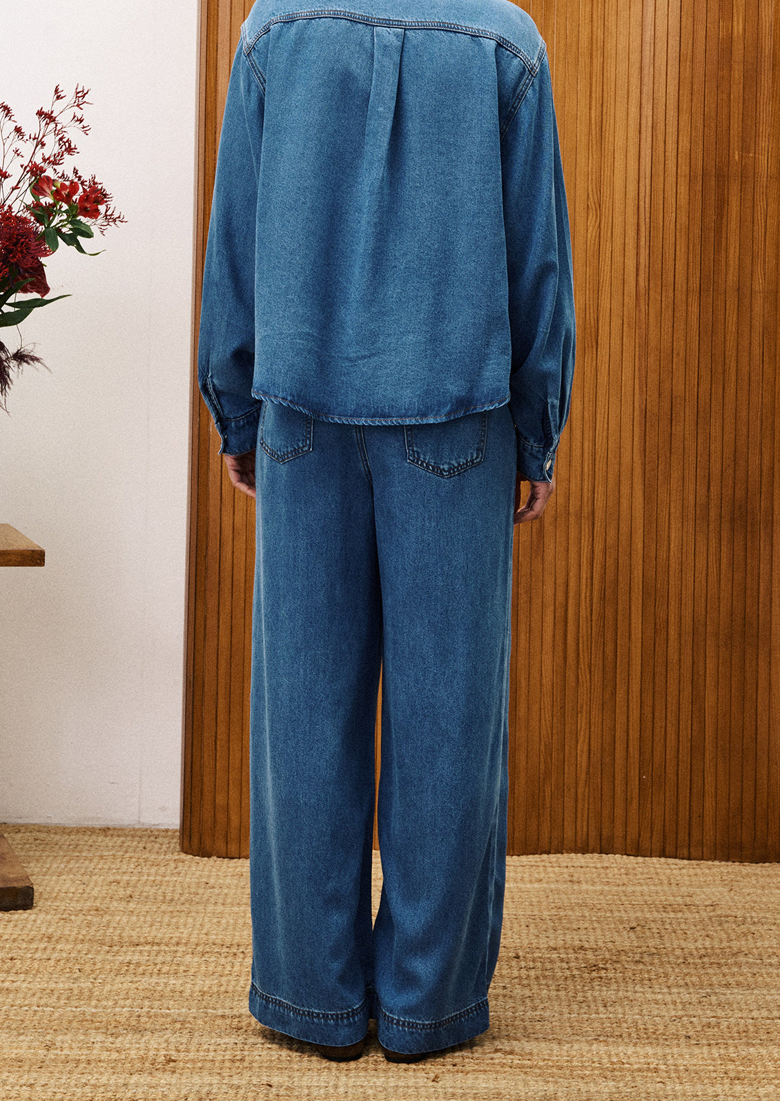 Person wearing a blue denim outfit standing against a wooden panel wall.
