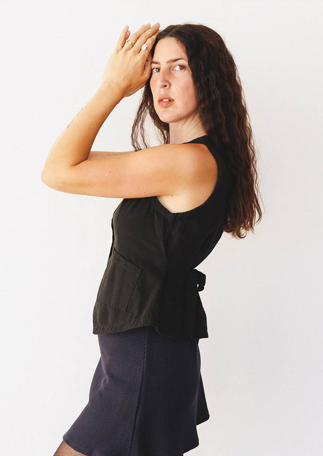 Woman wearing a black sleeveless top and navy skirt against a white background