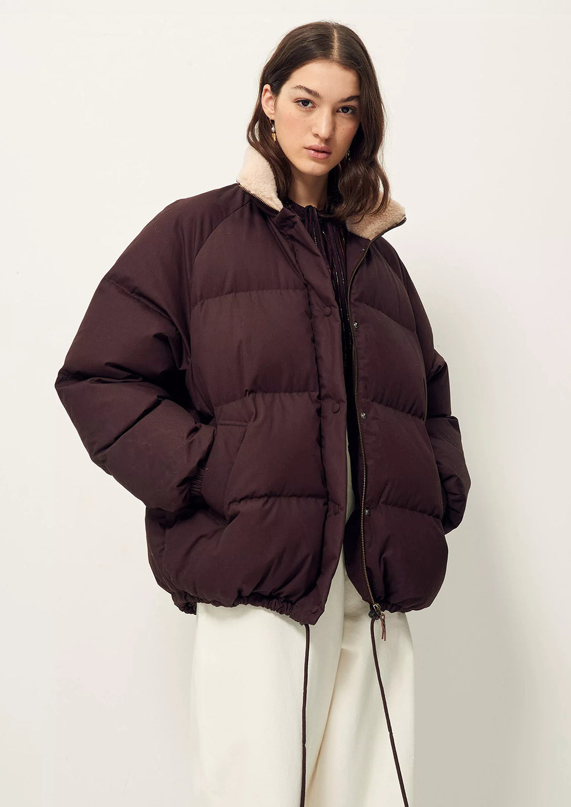 A woman wearing a burgundy puffer jacket with tan shearling collar.