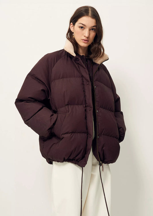 A woman wearing a burgundy puffer jacket with tan shearling collar.