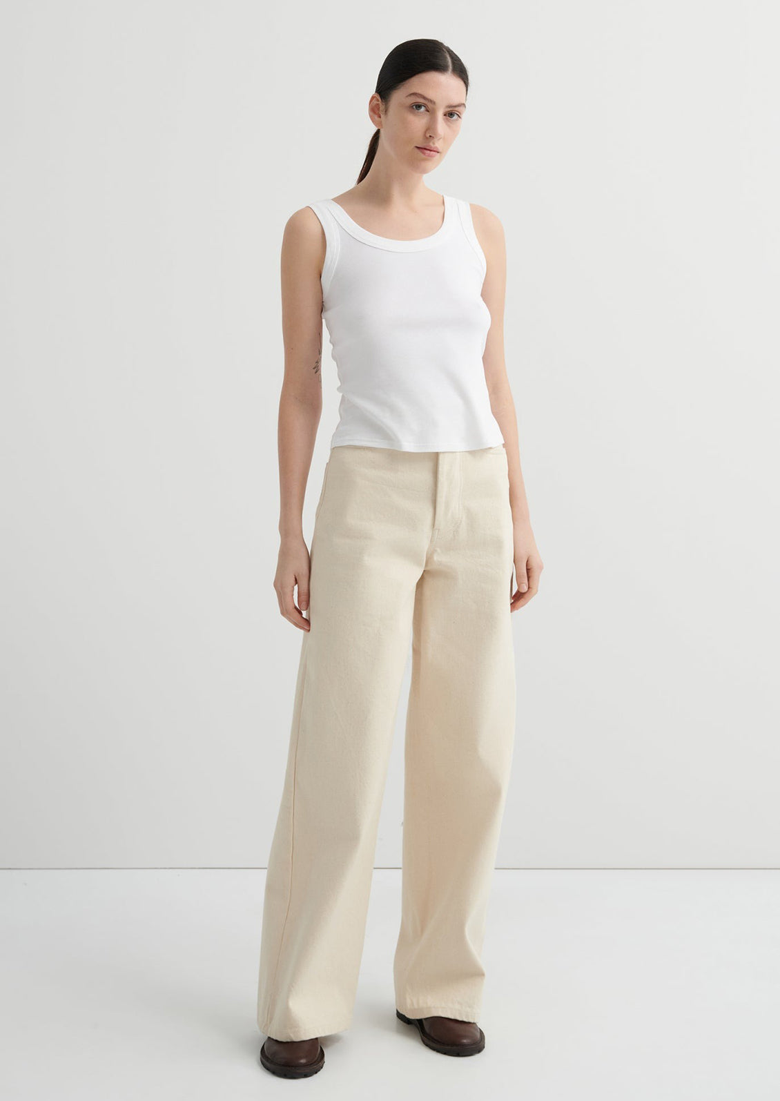 Woman wearing a white sleeveless top and beige wide-leg pants on a white background