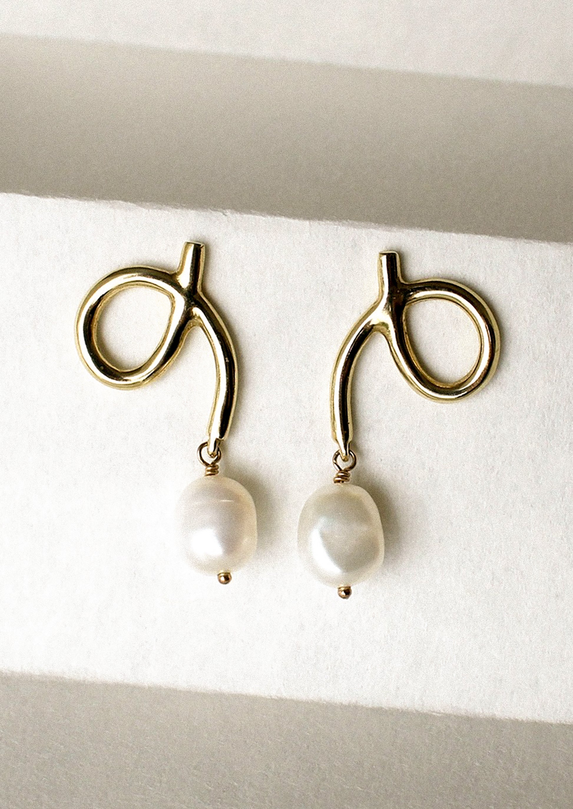 A pair of gold loop shaped earrings with dangling pearl bead.