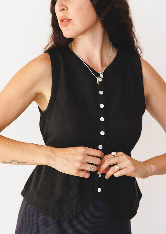 Woman wearing a black sleeveless top with buttons on a plain background
