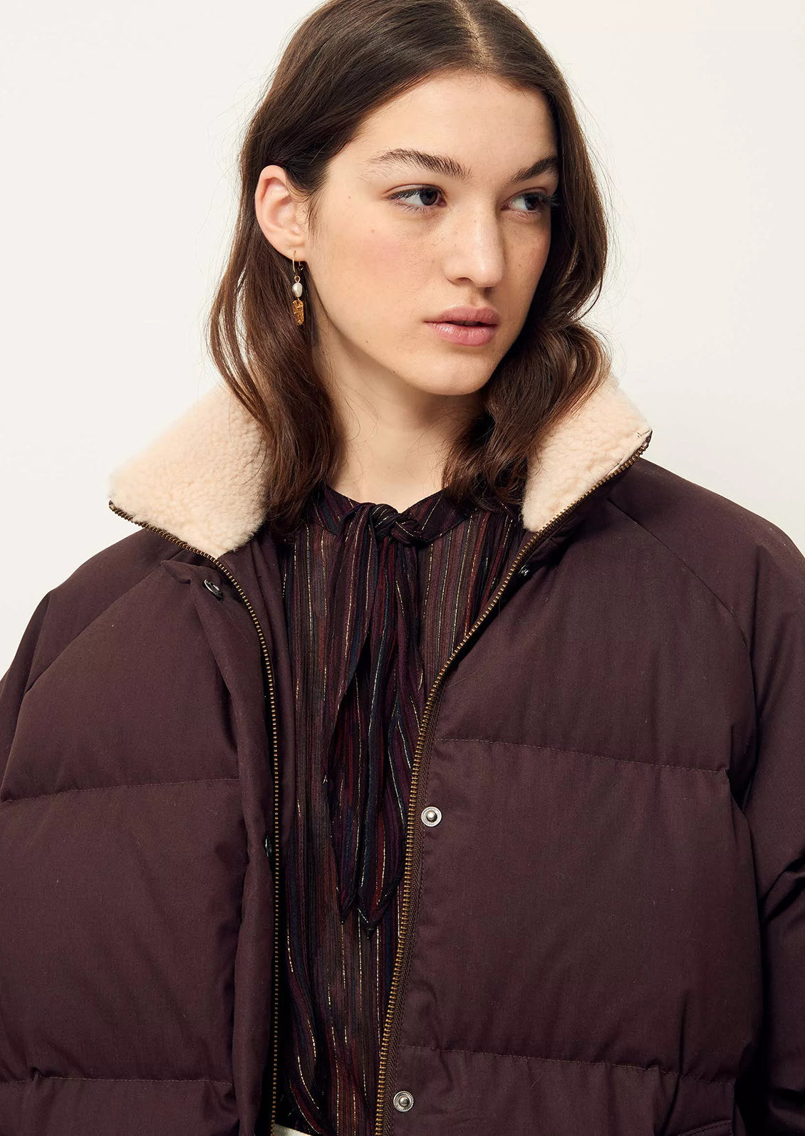 A woman wearing a burgundy puffer jacket with tan shearling collar.