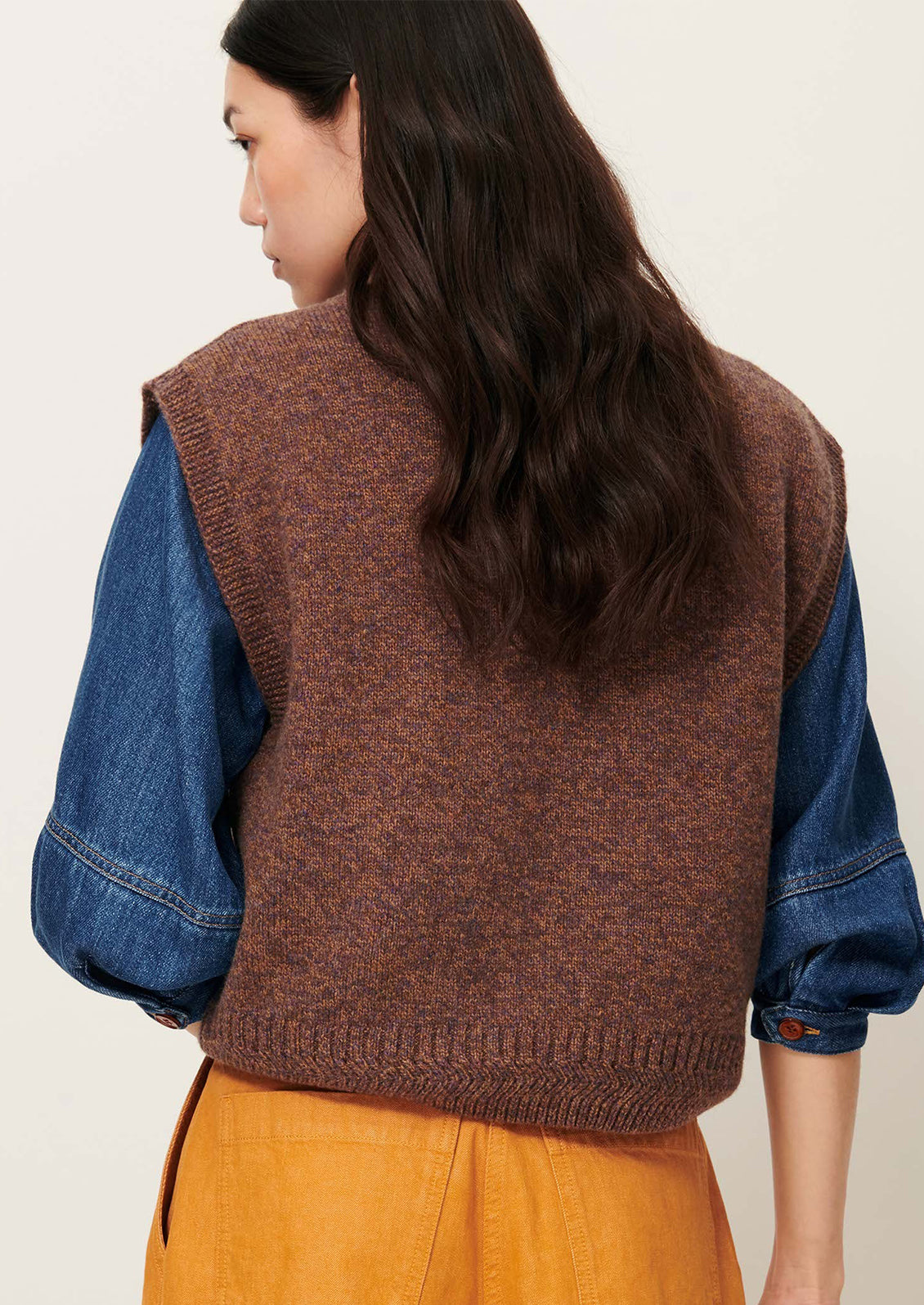 Woman wearing a brown knitted vest over a blue shirt.