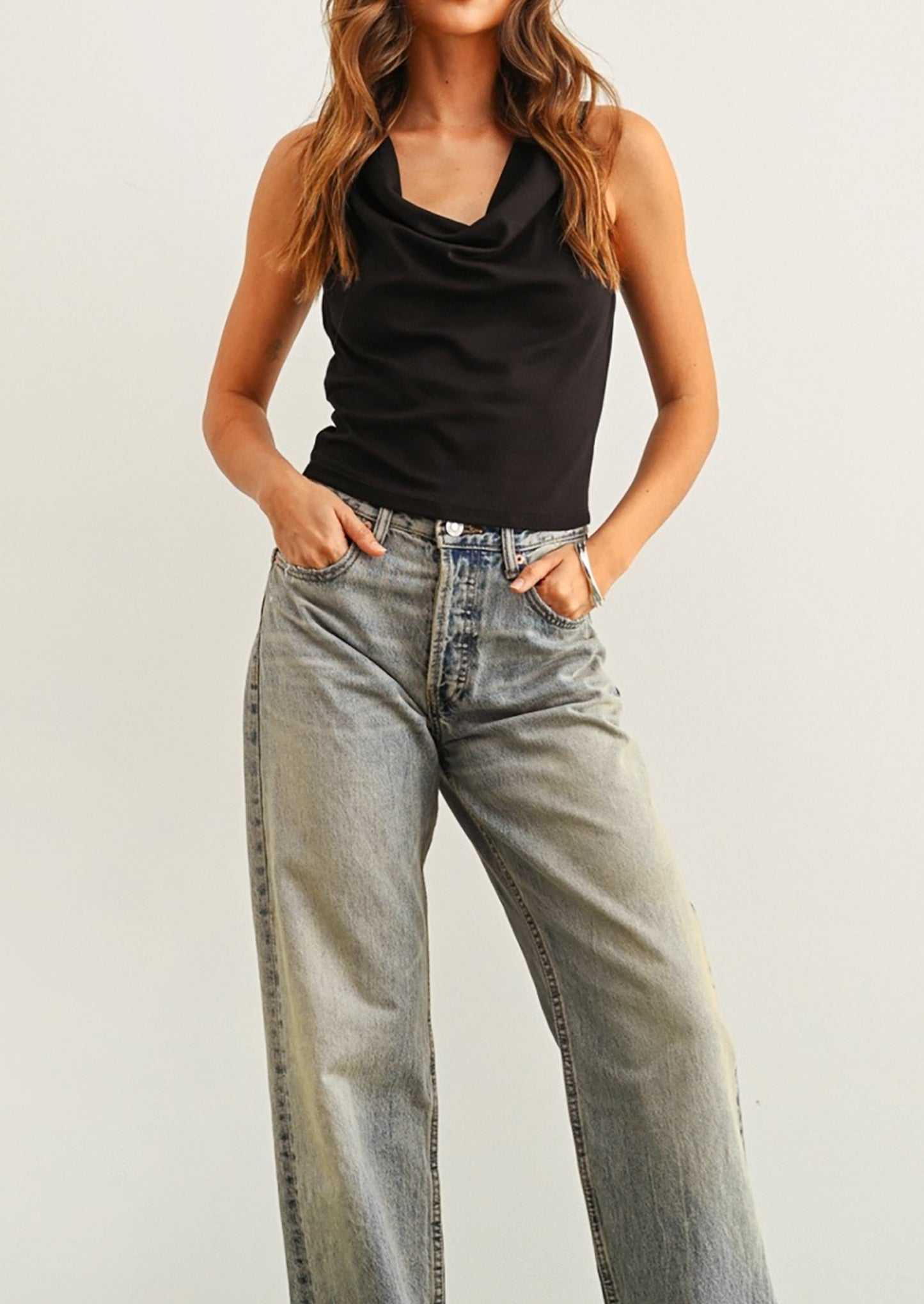 Person wearing a black sleeveless top and light blue jeans on a plain background