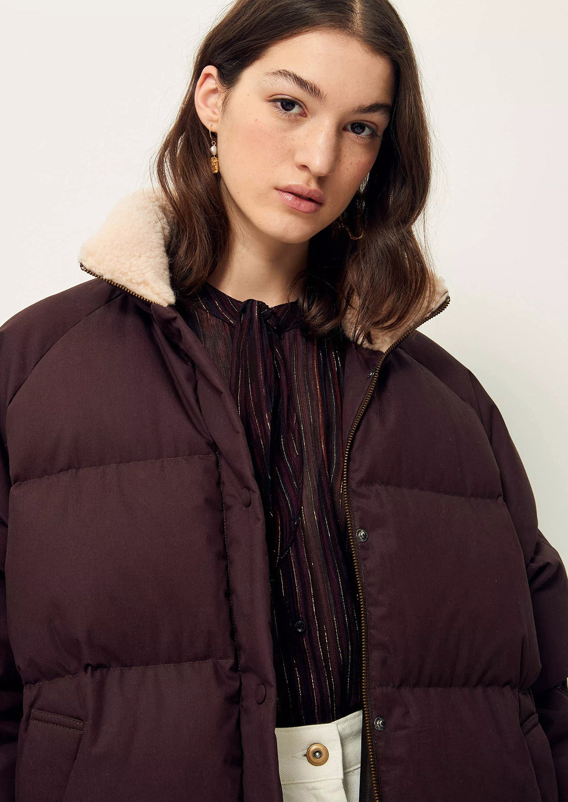 A woman wearing a burgundy puffer jacket with tan shearling collar.