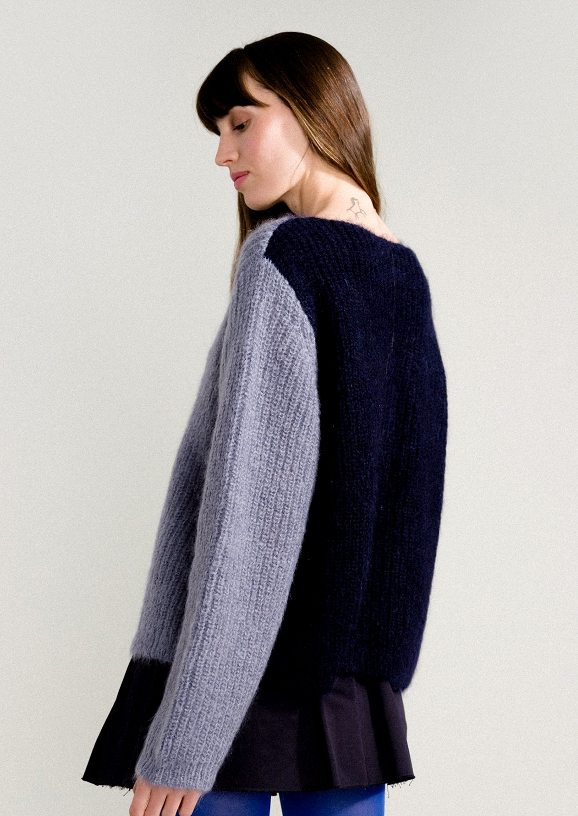 A woman wearing a long sleeve mohair sweater with two-tone colorblocking in dusty blue and navy.