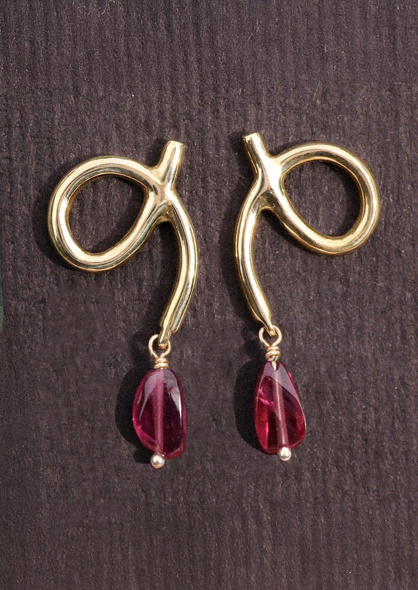 A pair of gold loop shaped earrings with dangling garnet bead.