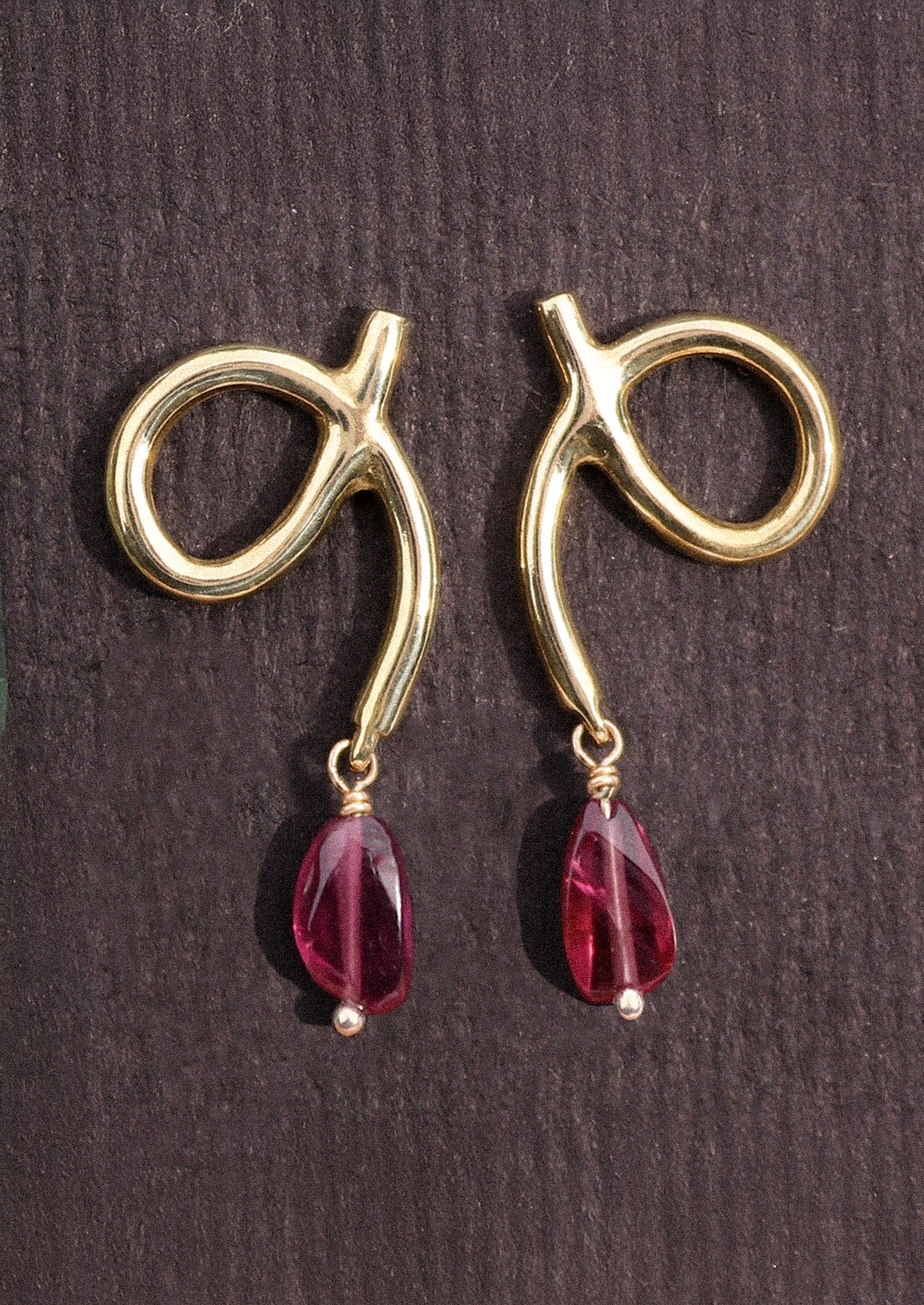A pair of gold loop shaped earrings with dangling garnet bead.