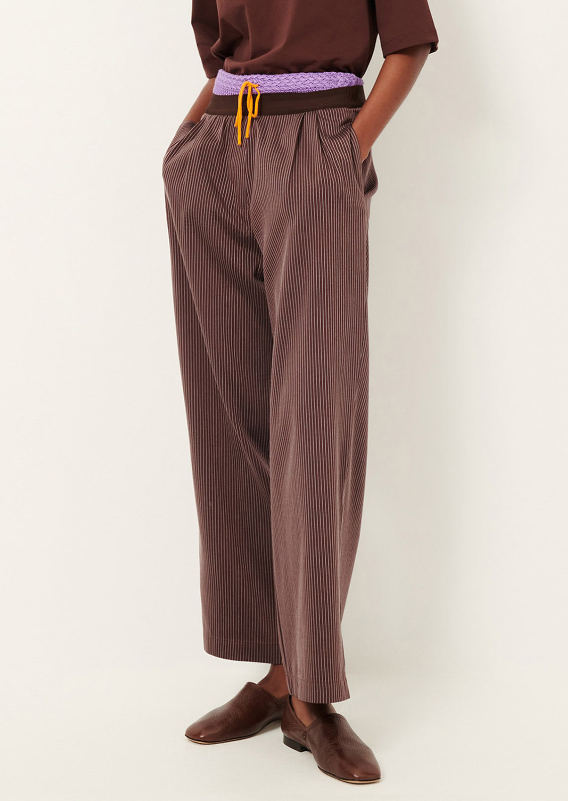 Person wearing brown striped pants with a purple belt on a white background