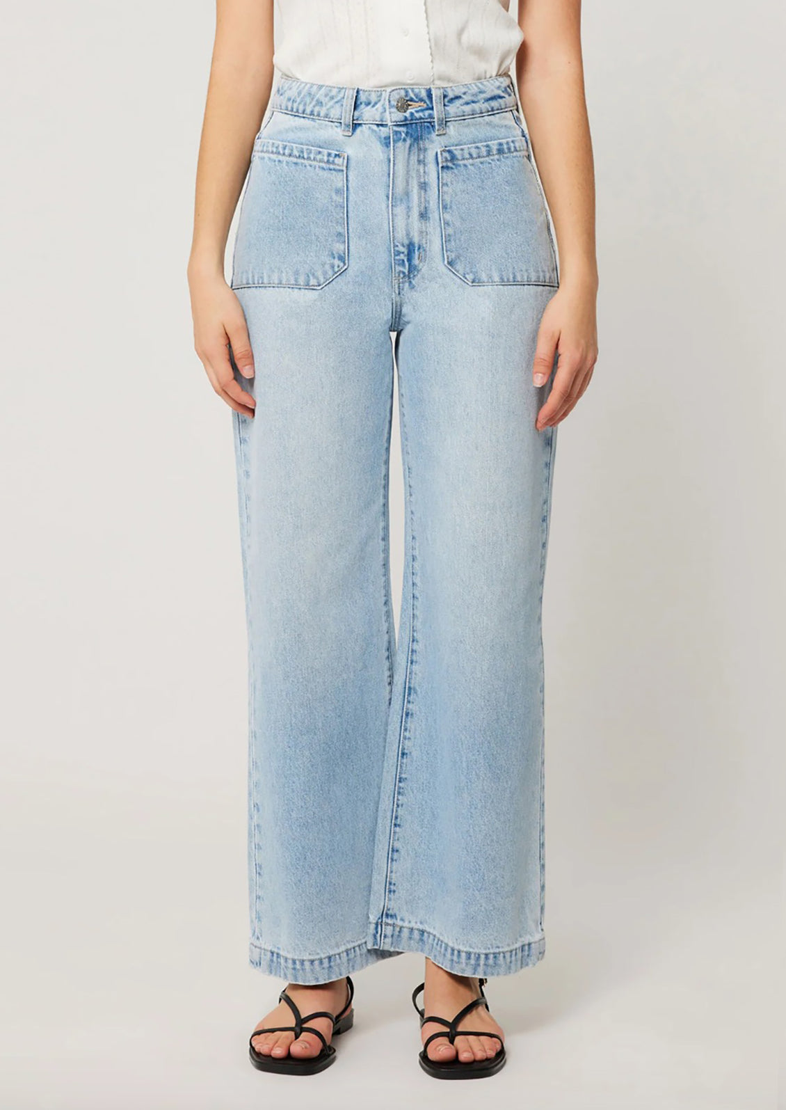 A person wearing a pair of light blue denim wide leg jeans with patch pockets at hips. 