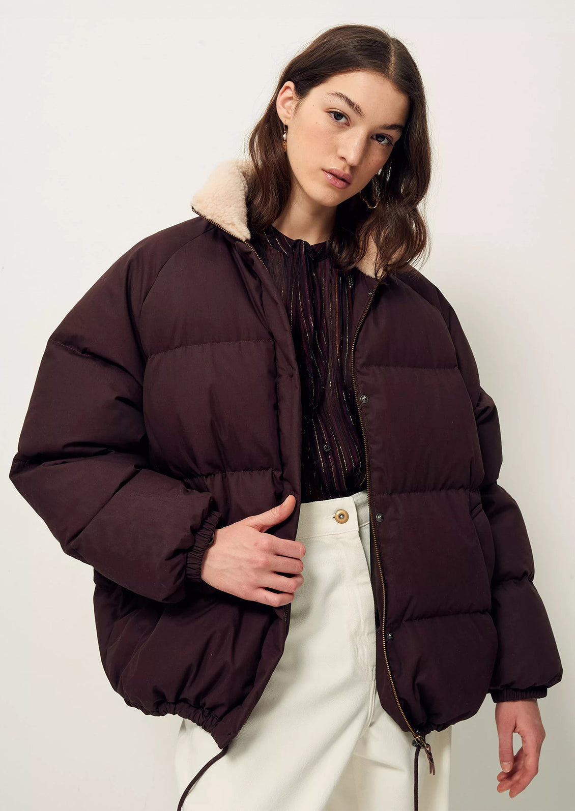 A woman wearing a burgundy puffer jacket with tan shearling collar.