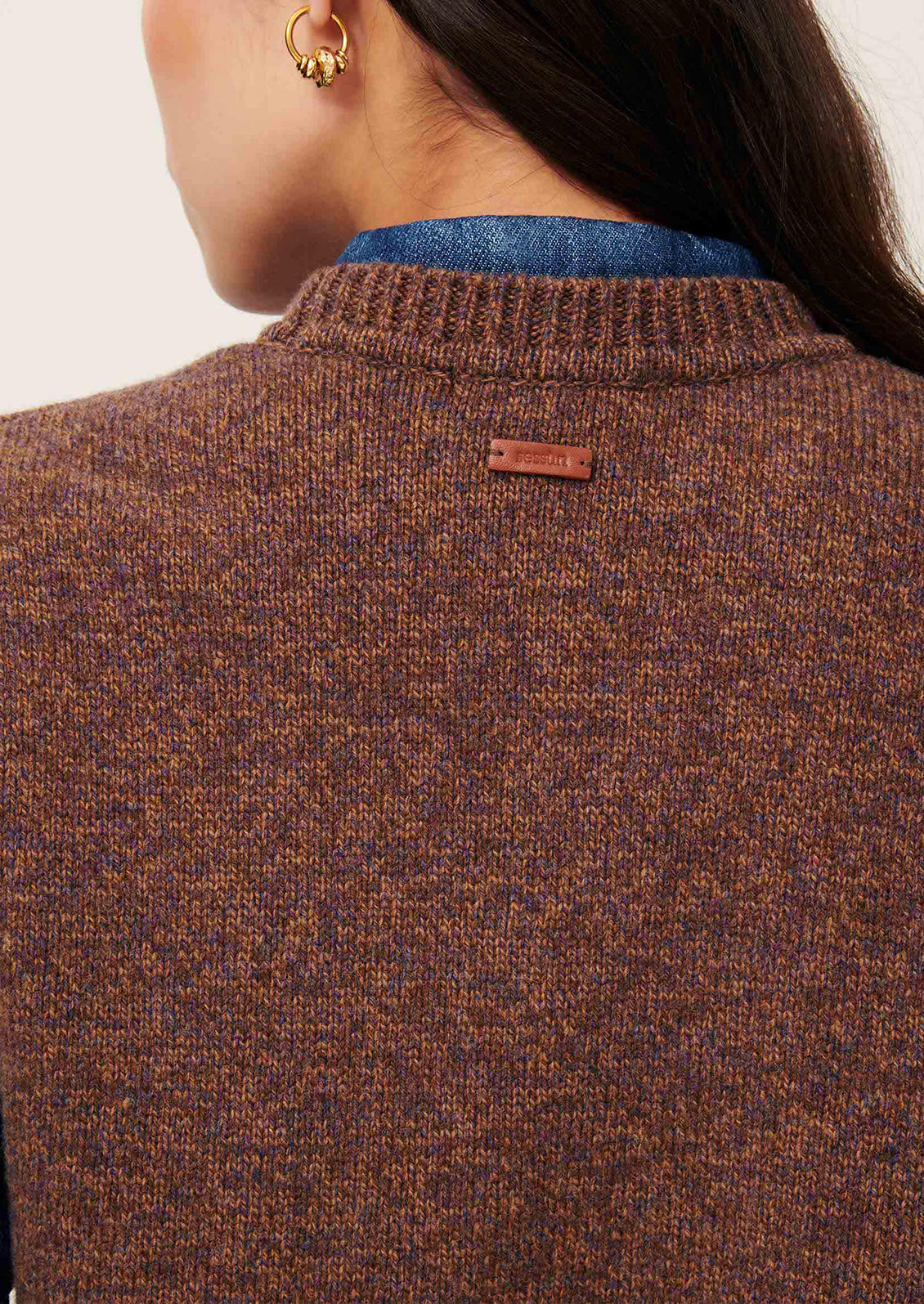 Woman wearing a brown knitted vest over a blue shirt.