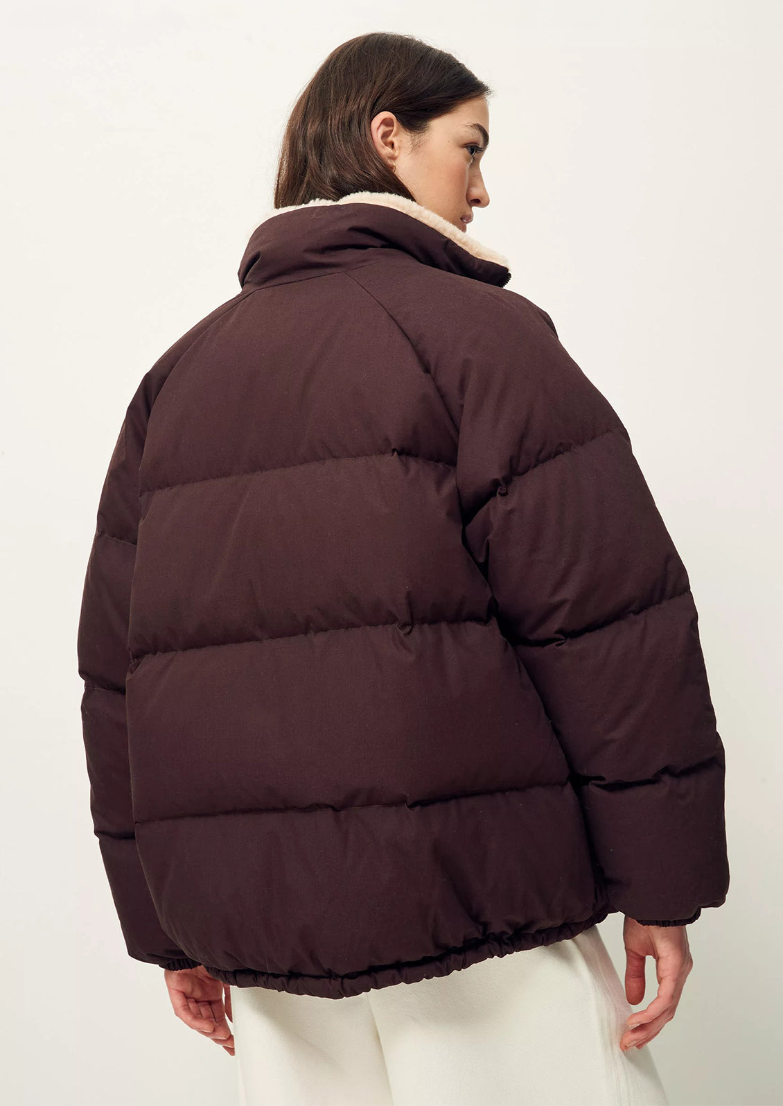 A woman wearing a burgundy puffer jacket with tan shearling collar.