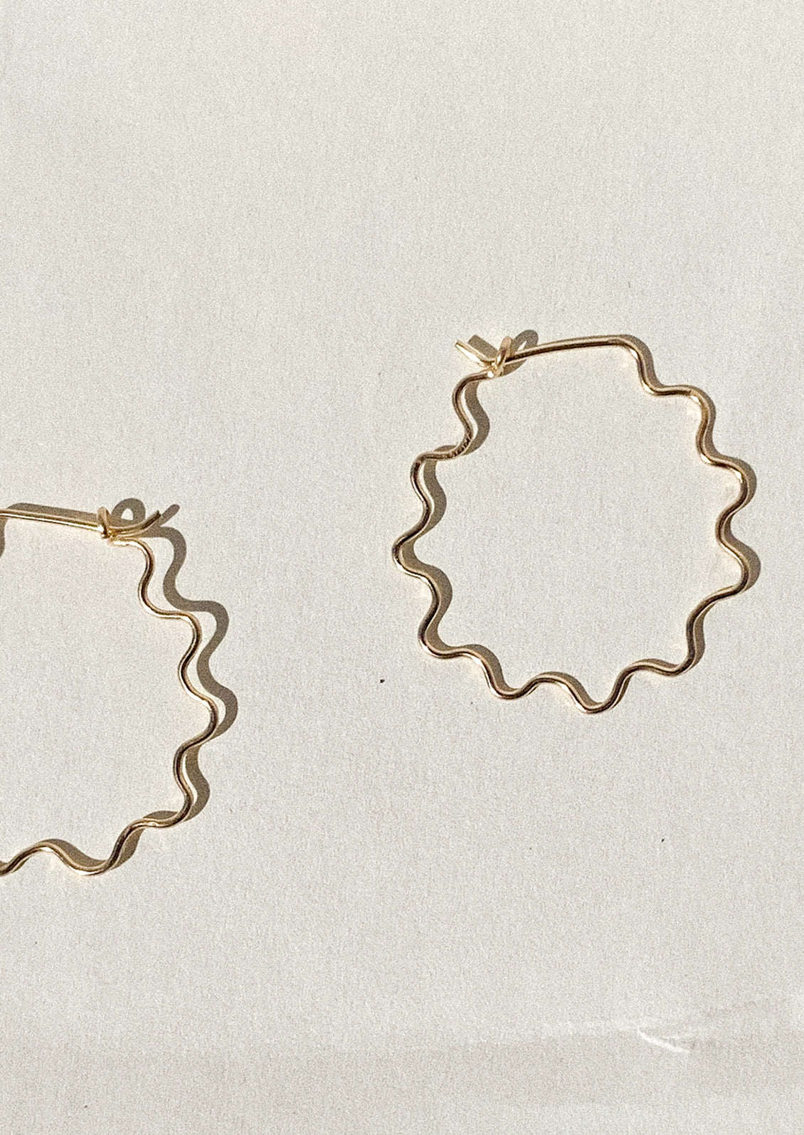 Gold hoop earrings with a wavy squiggle shape on a light beige background.
