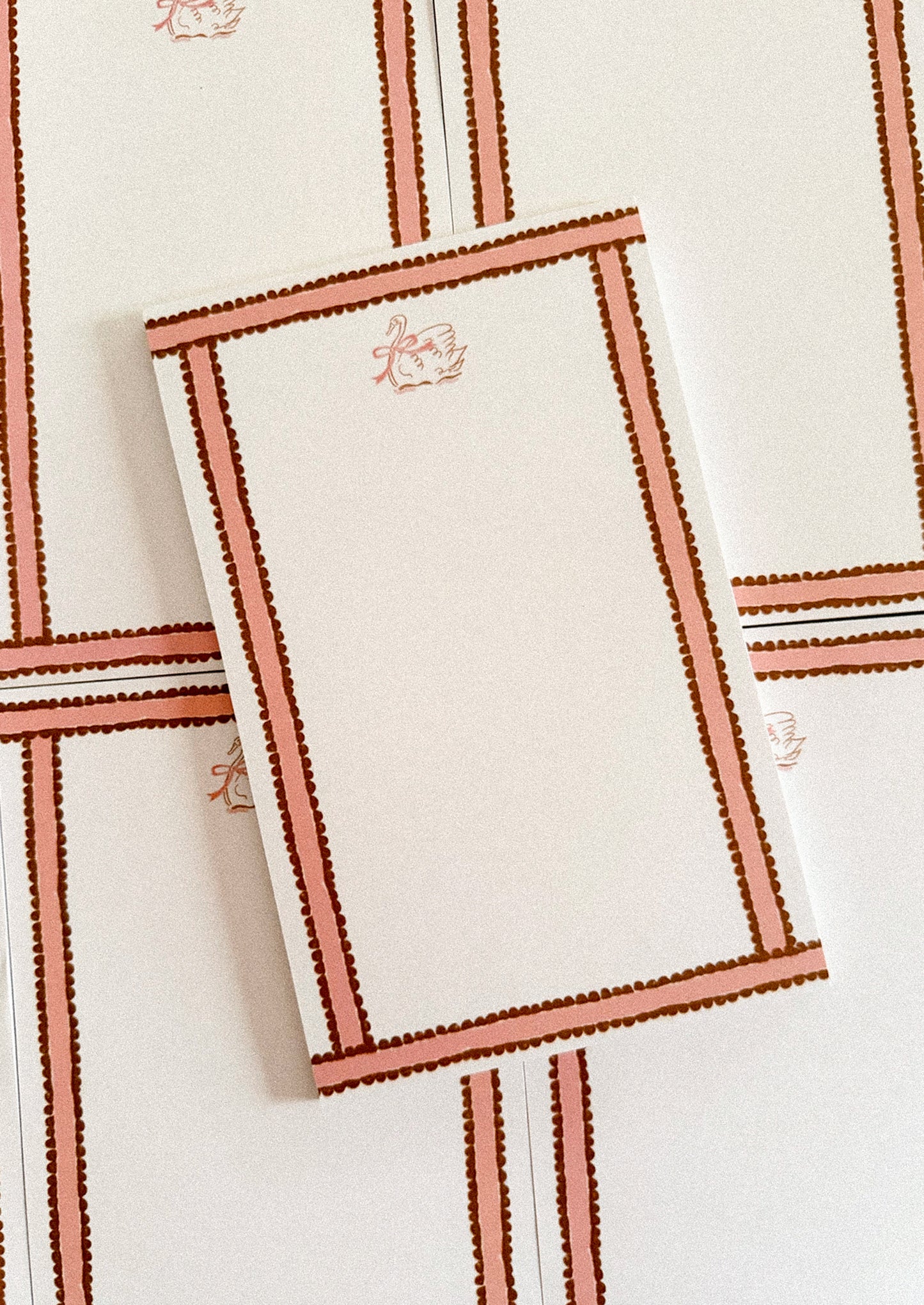 Rectangular notepad with swan motif and decorative border.