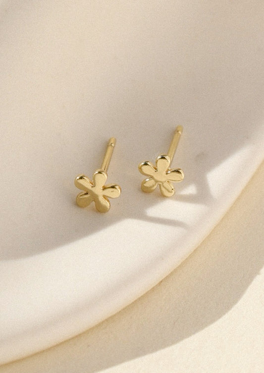 Gold flower earrings on a beige surface
