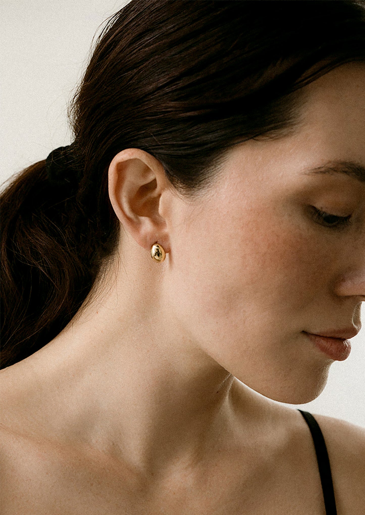 Close-up of a woman wearing a gold earring with a neutral background