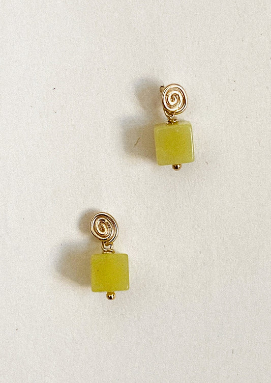 Pair of gold earrings with green square beads on a light background