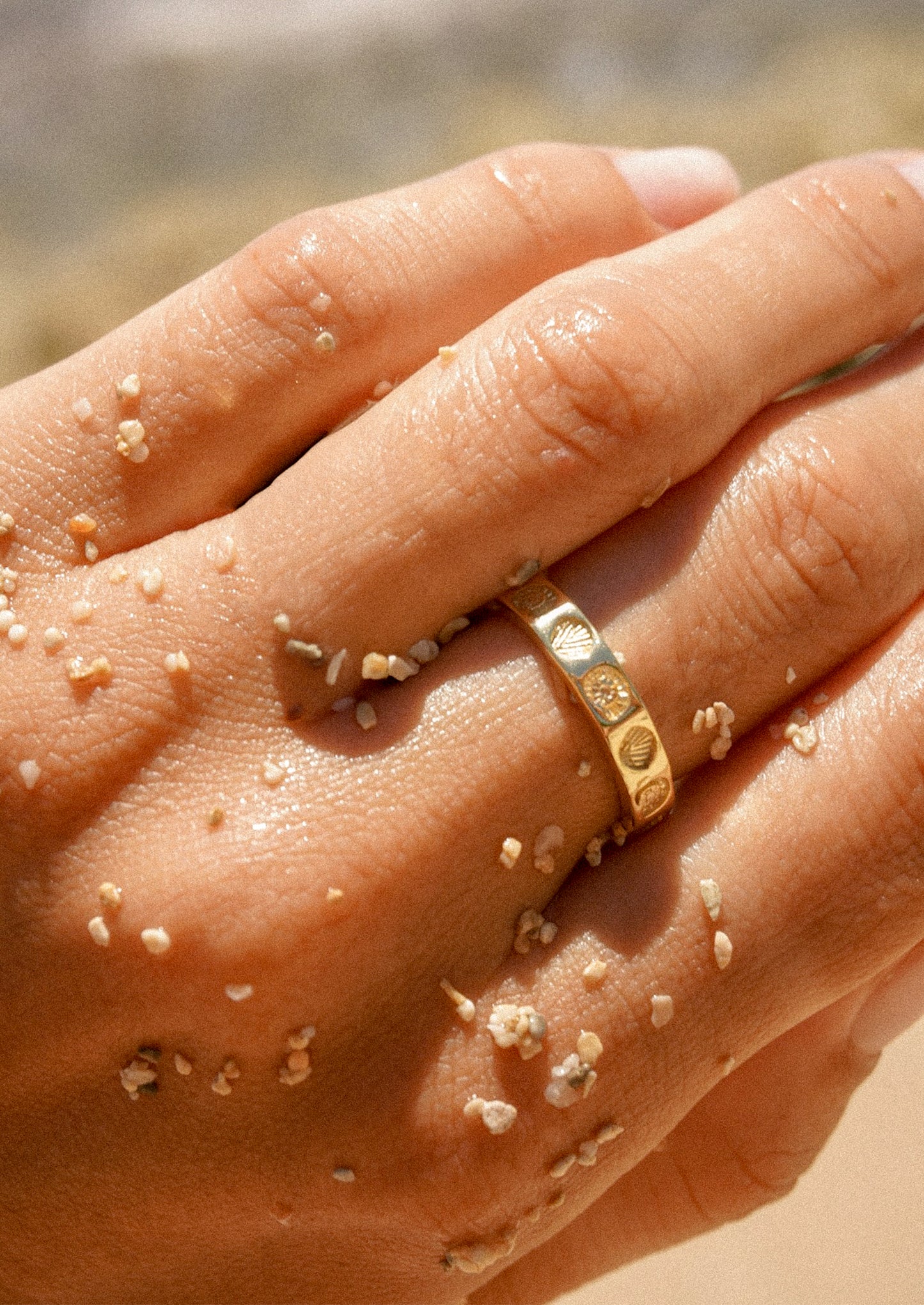 A close up of a person wearing a shell imprint ring in gold.