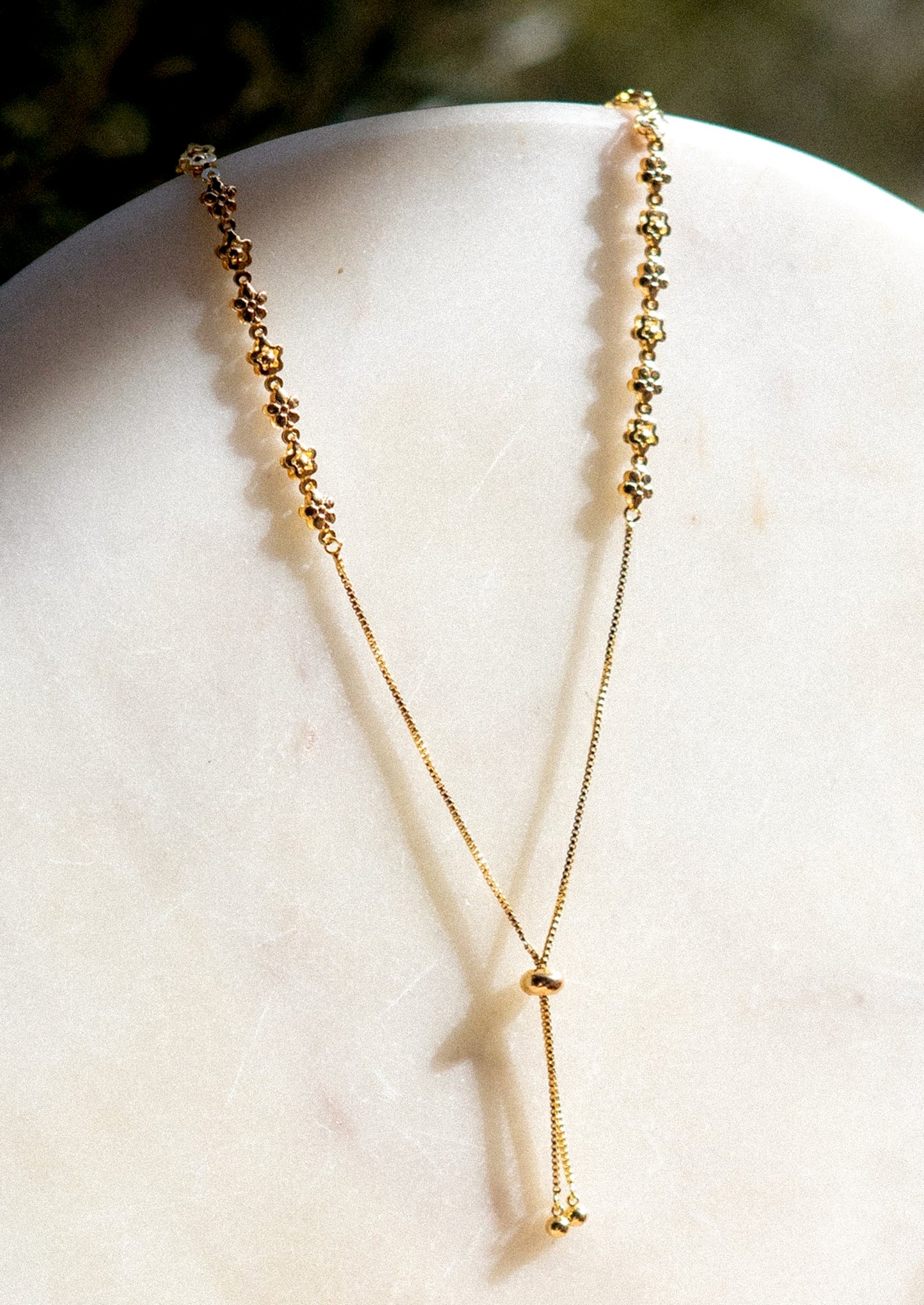 A lariat style necklace in gold with flower detail.