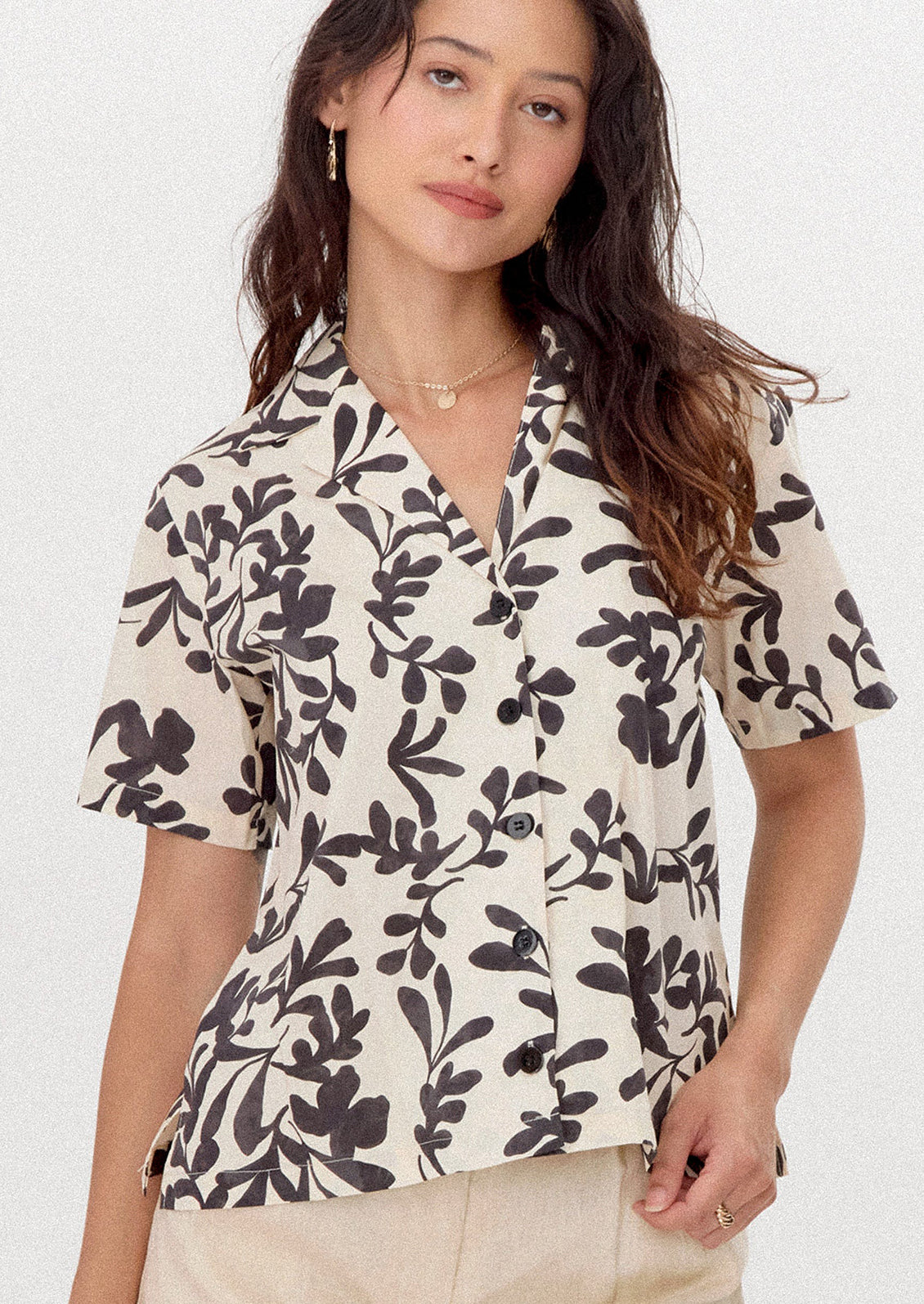 A person wearing a white short sleeve shirt with black leafy floral print.