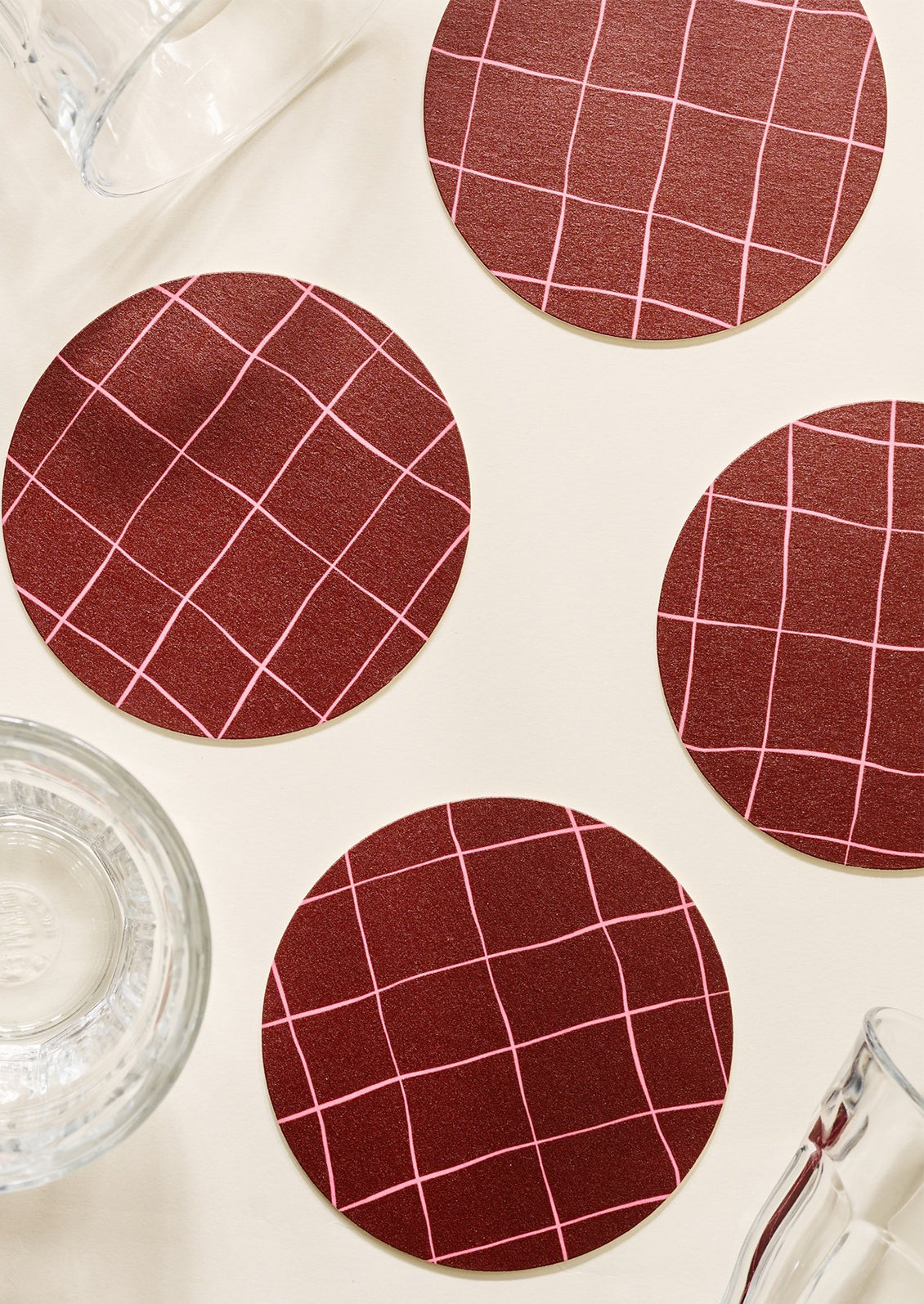 A set of maroon coasters with pink windowpane pattern.