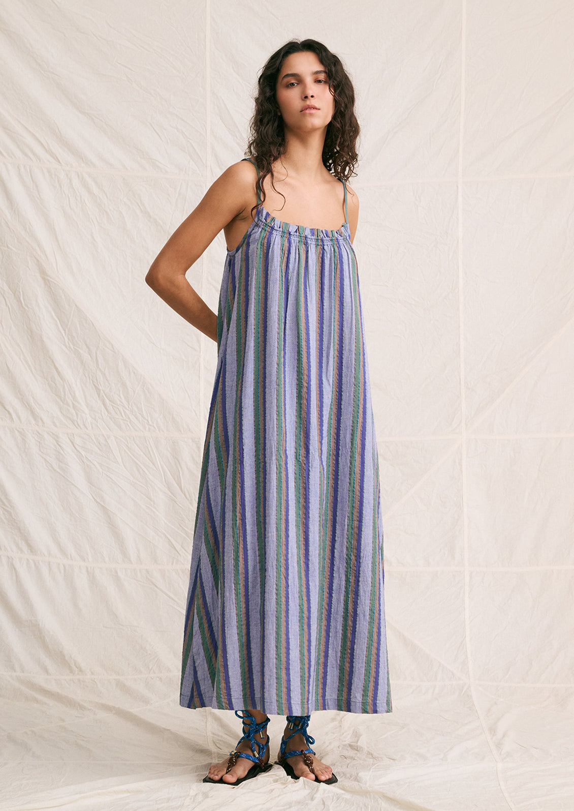 A woman wearing a chambray sundress with green, brown and blue stripe pattern.