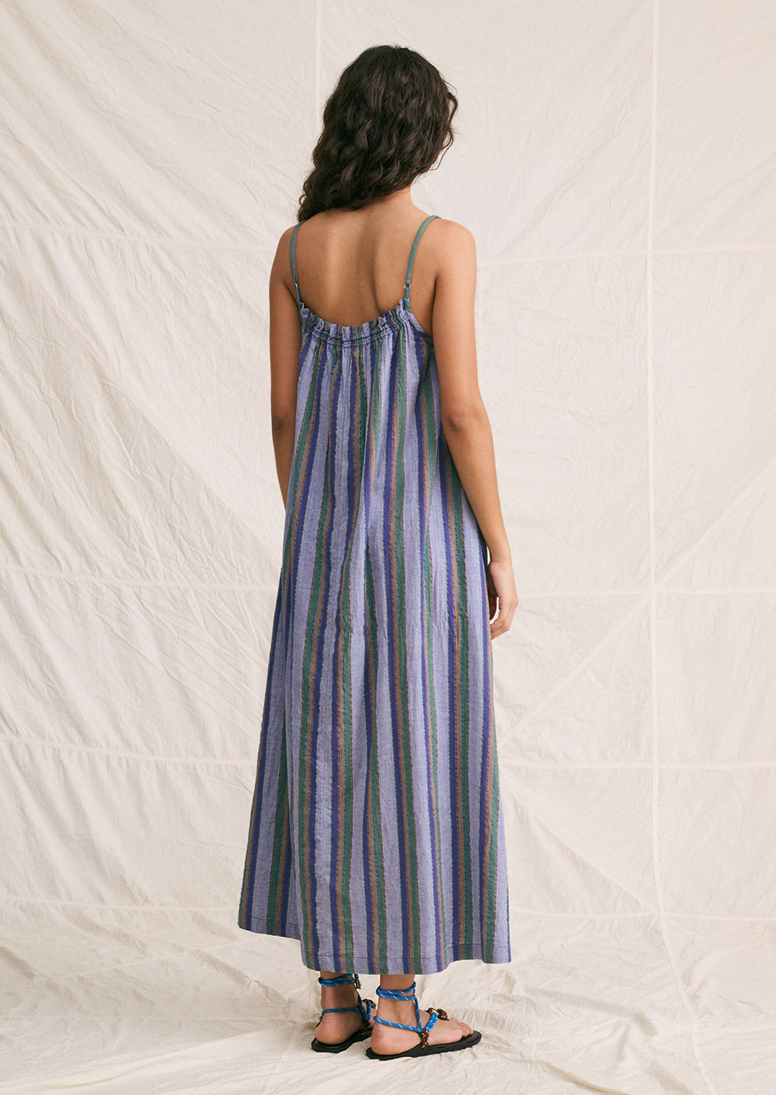 A woman wearing a chambray sundress with green, brown and blue stripe pattern.
