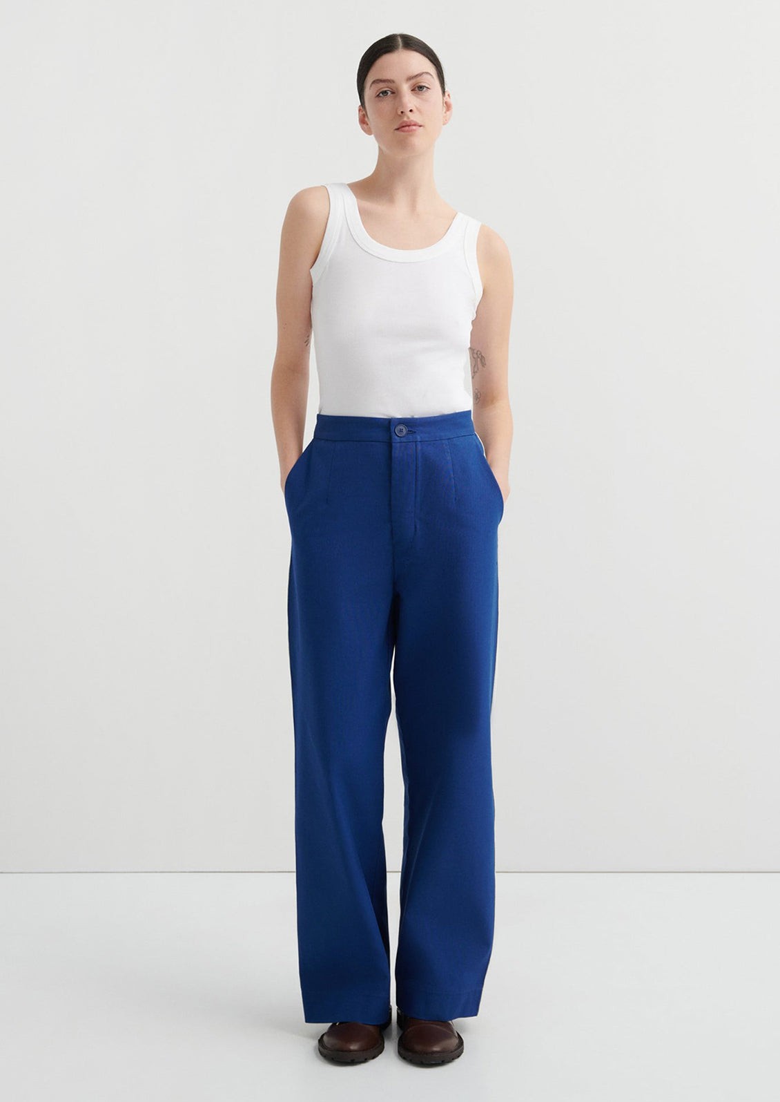 Woman wearing a white tank top and blue pants on a white background