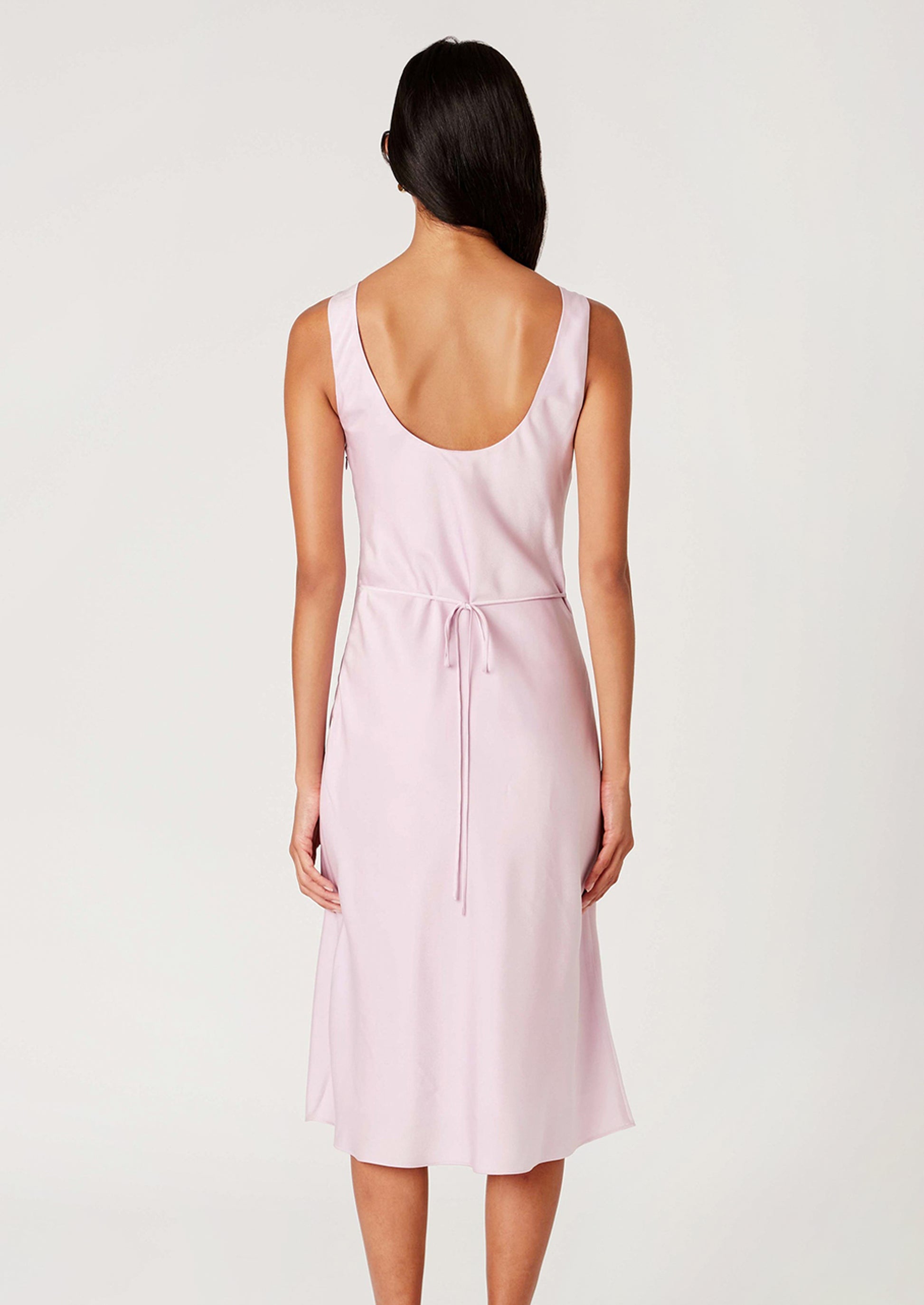 A woman wearing a satin v-neck sleeveless dress in ice pink.