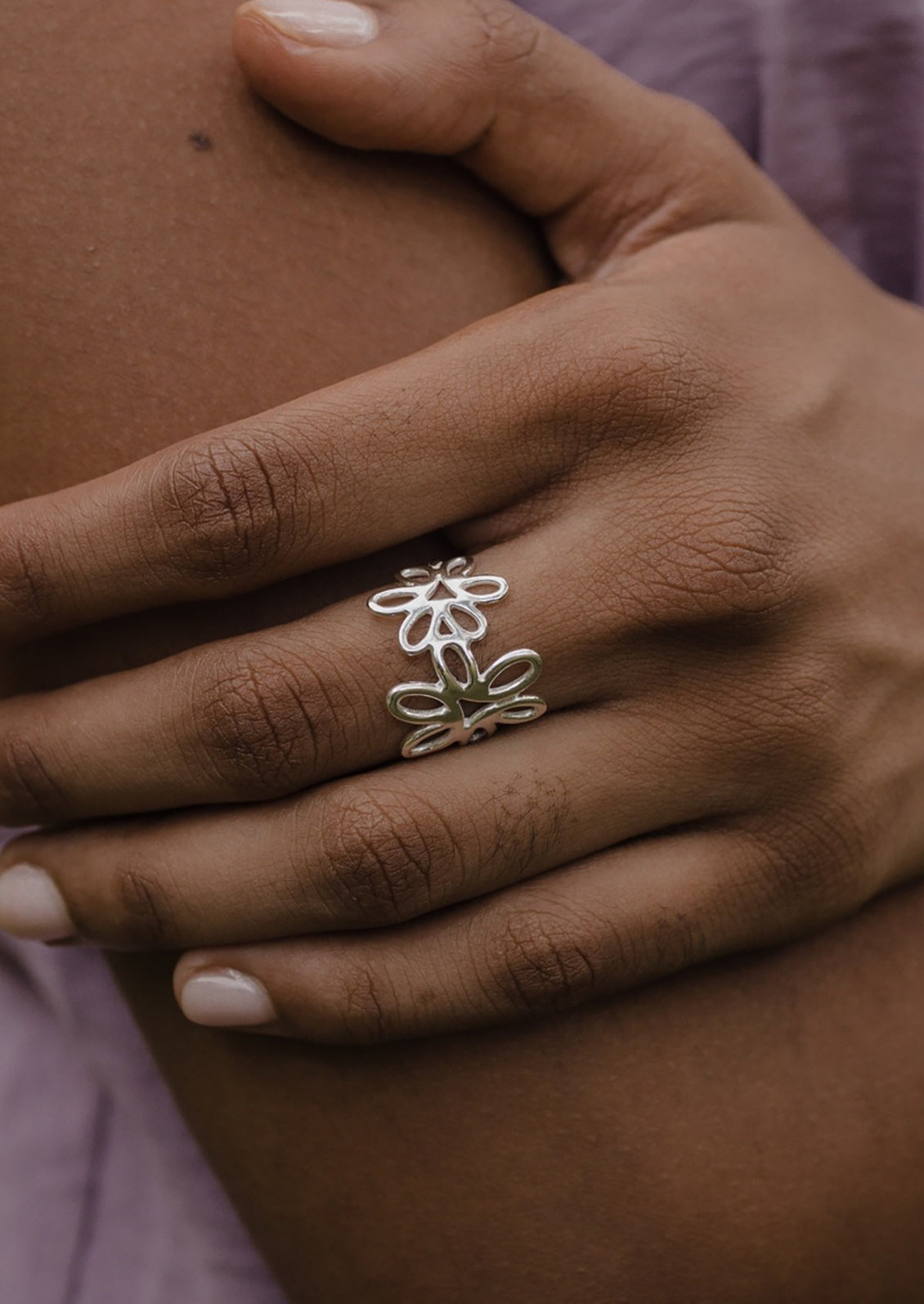 A sterling silver ring with a floral design on the top part, worn on a person's finger.