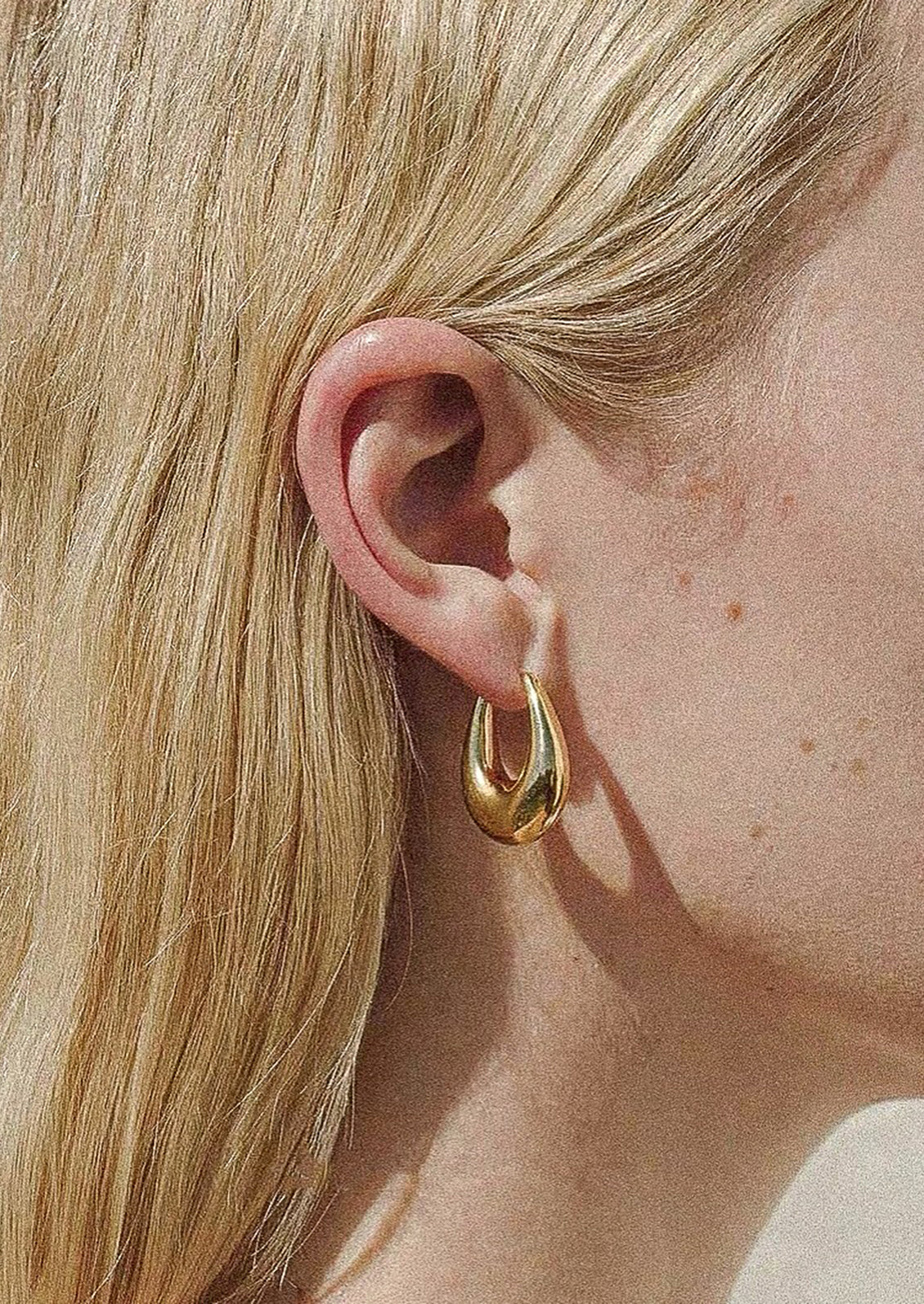 A person wearing a pair of bold chunky oblong shape earrings in gold.