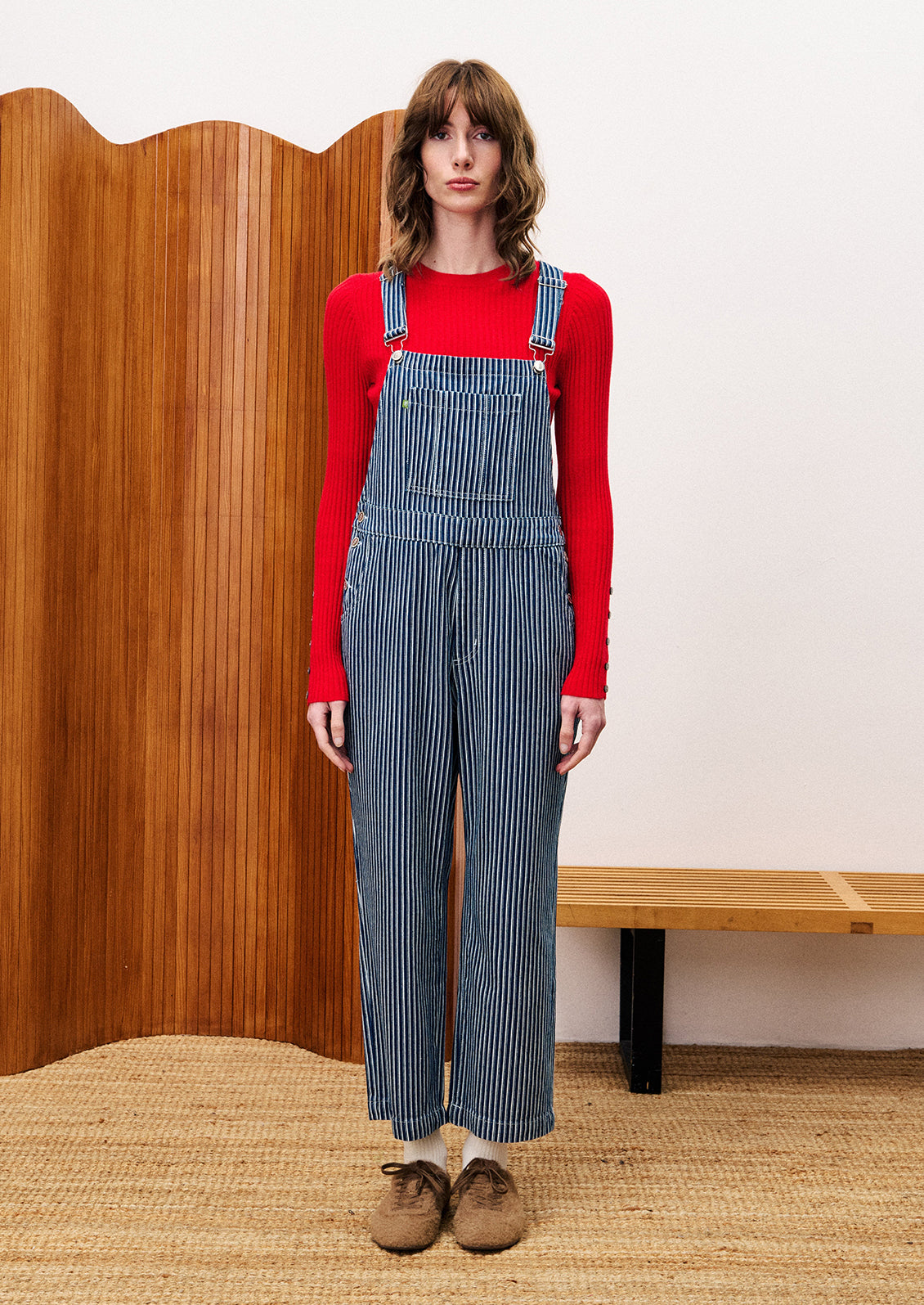 Person wearing a red sweater and blue striped overalls.