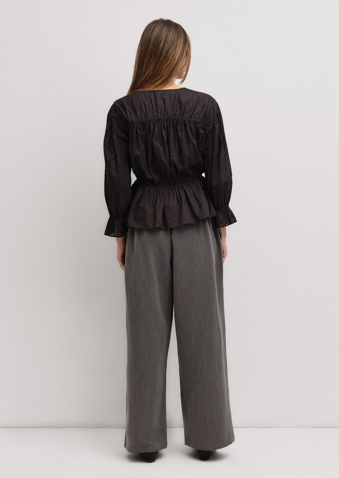 A woman wearing a black cotton blouse with ruching and bow tie detail at front.