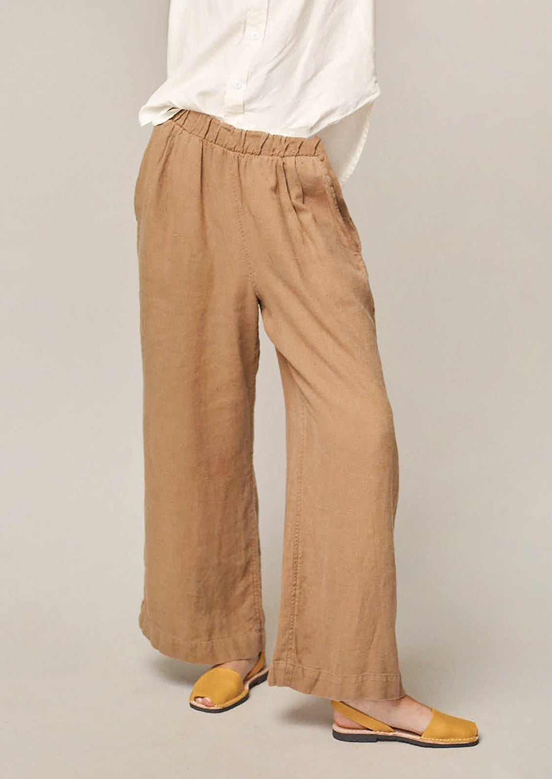 A person wearing a pair of flowy hemp pants in tan.